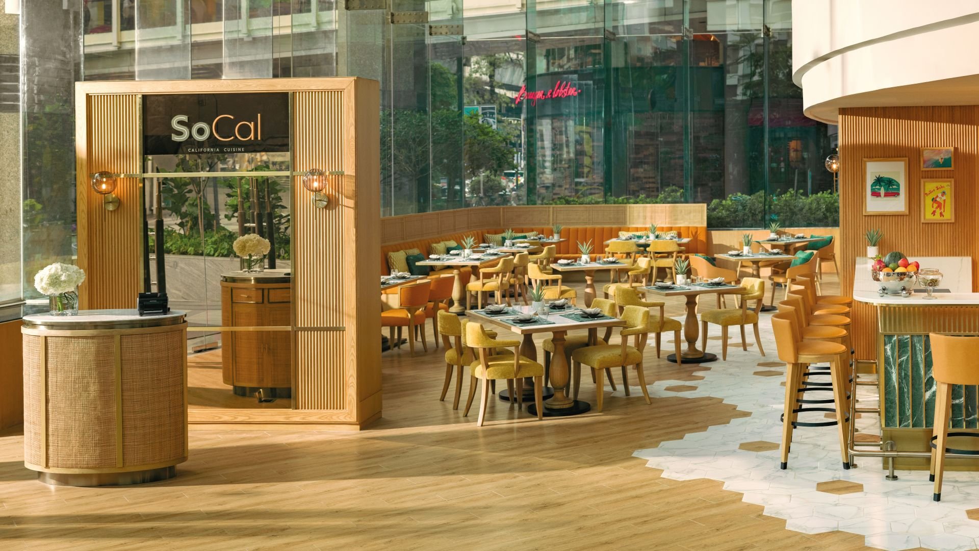 Inside a modern restaurant with wooden accents, yellow and green chairs, tables set with plates and napkins, and large glass windows showing street view.
