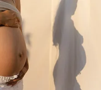 Close-up of a pregnant woman holding her belly, casting a shadow on the wall.