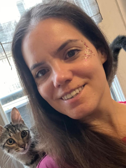 Une femme souriante maquillée près de l'œil, accompagnée d'un chat tacheté.