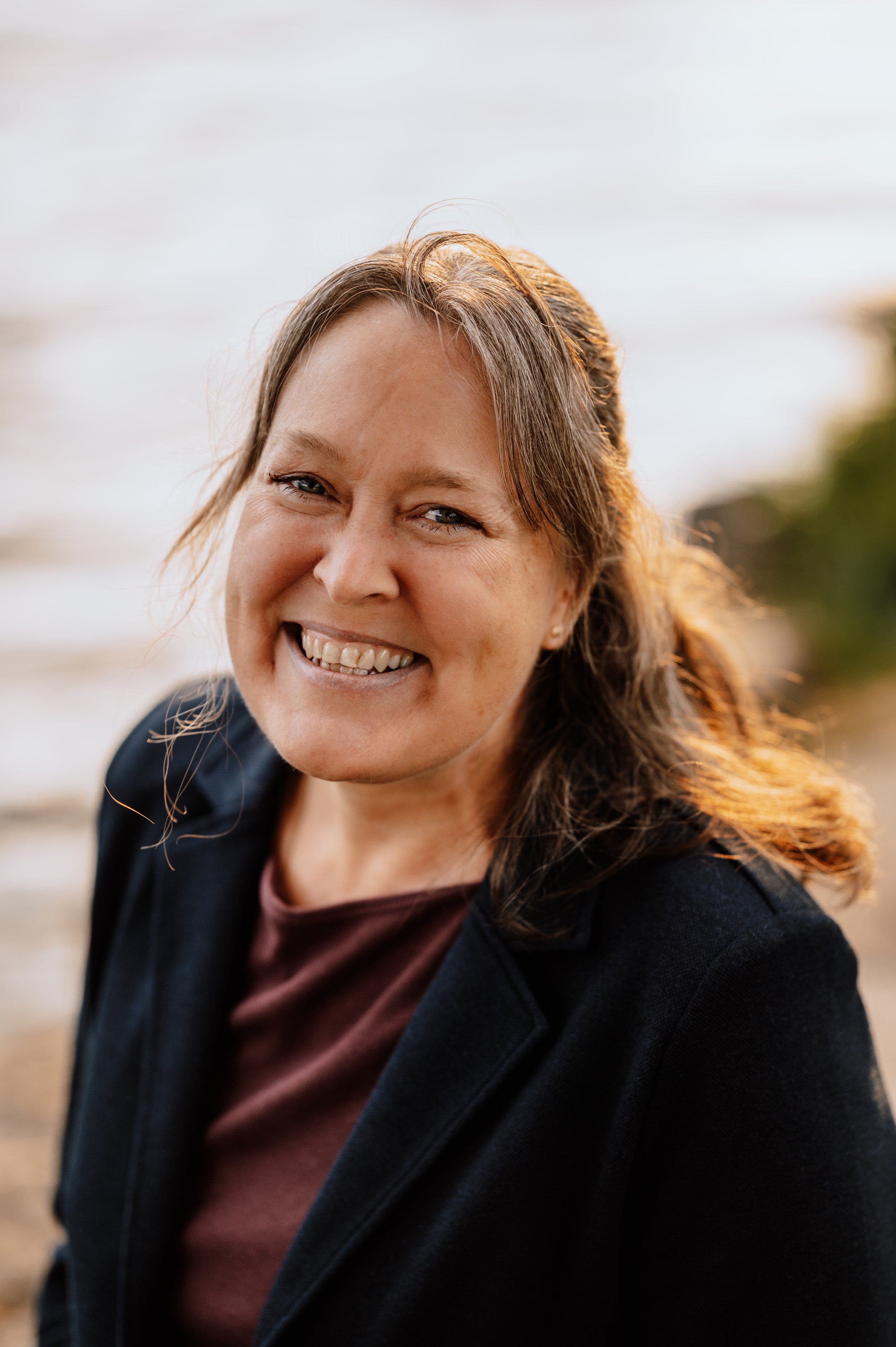 Nahaufnahme einer lachenden Frau mit braunem Haar, am Strand bei Sonnenuntergang.