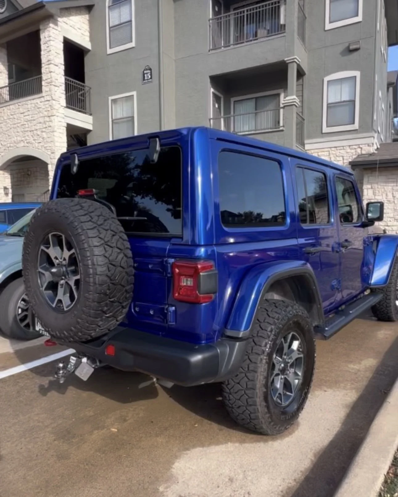 Blue Jeep Wrangler parked in a residential parking lot with a spare tire on the back.