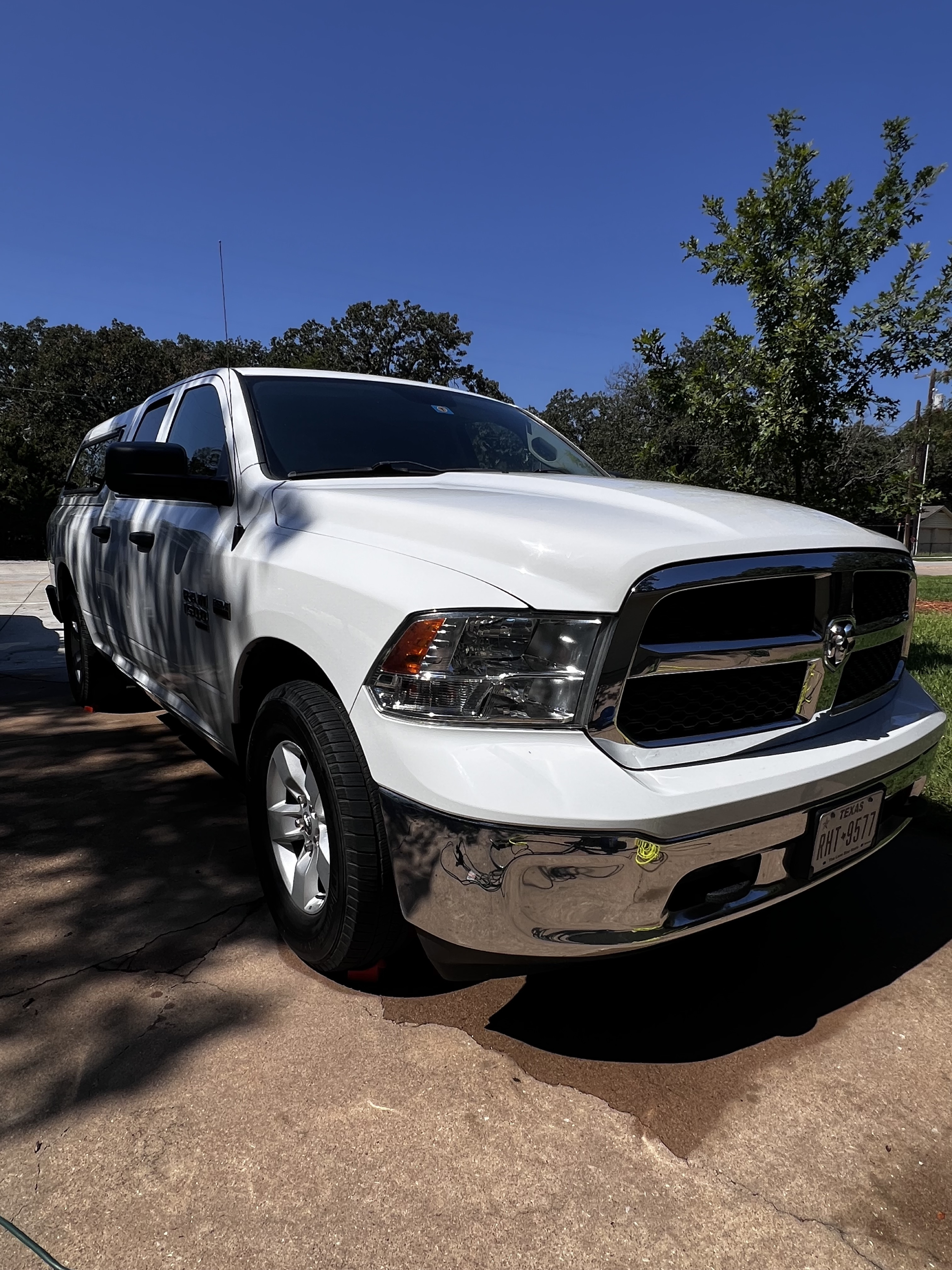 A white Dodge Ram pickup truck parked on a driveway with shadowed trees and a blue sky in the background.