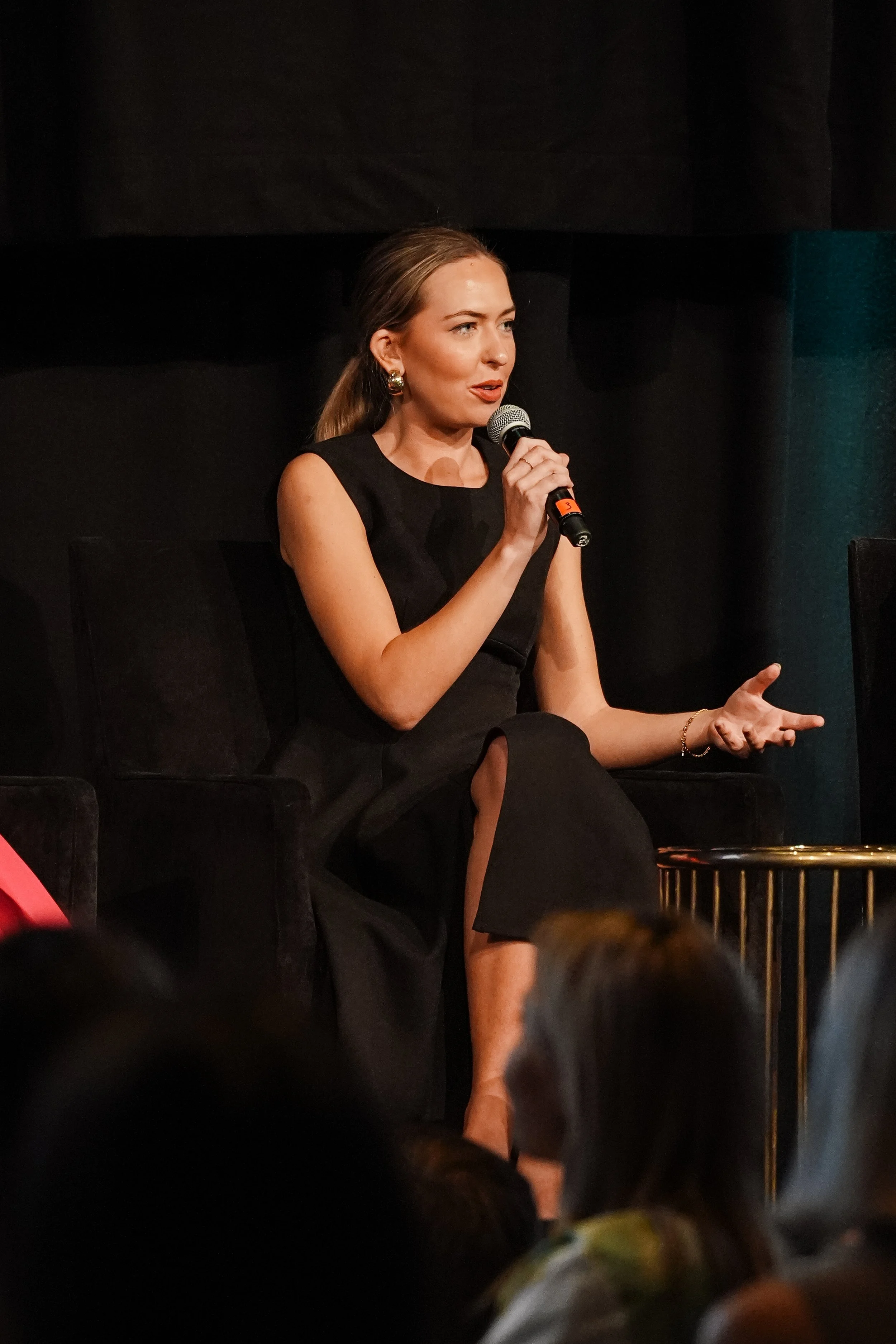 Anja Christoffersen speaking on stage at a live event, holding a microphone and addressing an audience