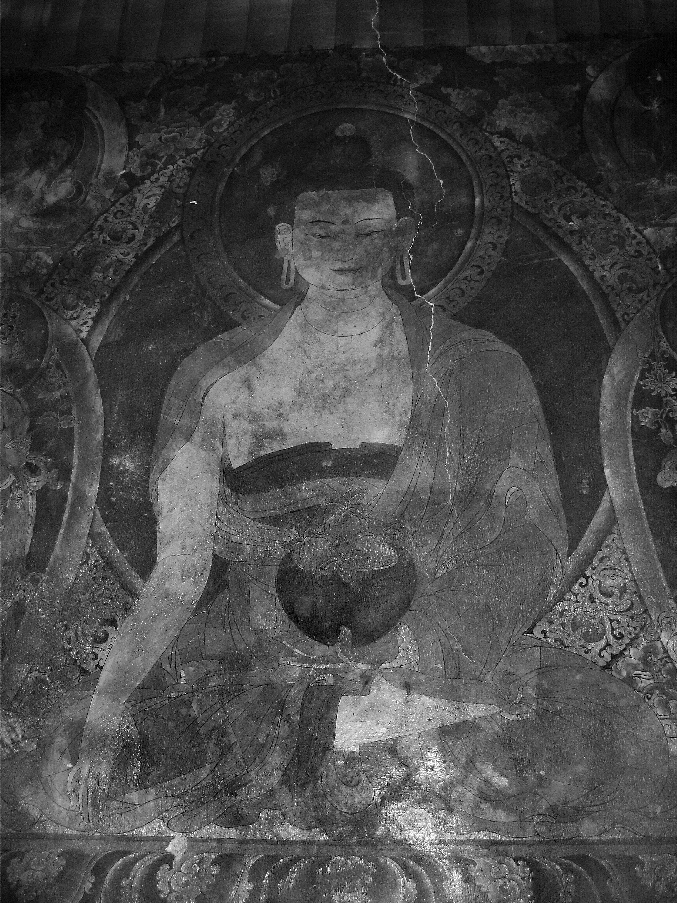 Black and white image of a traditional religious mural of a serene female figure, possibly a goddess or bodhisattva, with a halo around her head, holding a vessel with flowers, surrounded by intricate decorative patterns.
