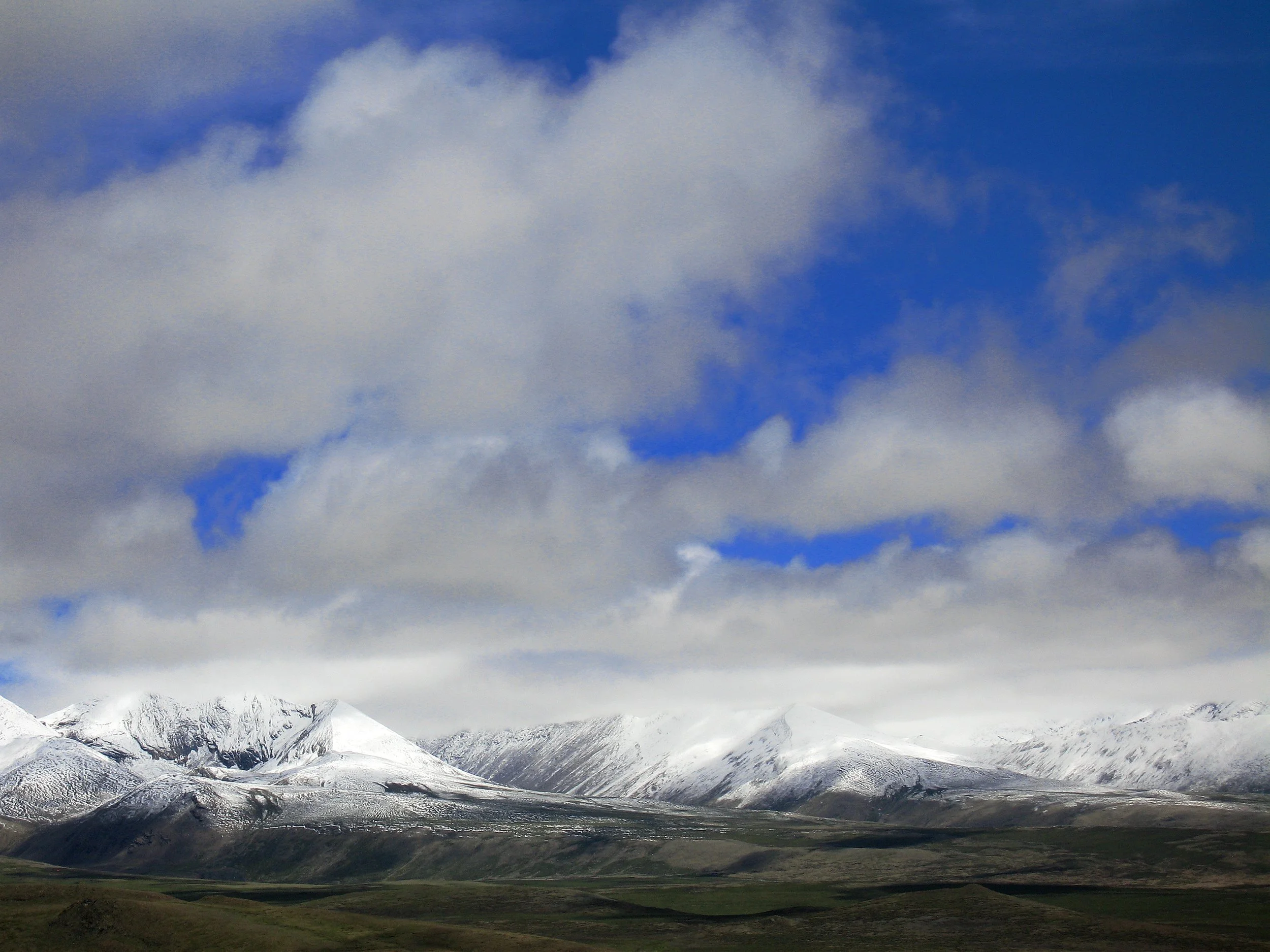 Snow-capped mountains under a partly cloudy sky with patches of blue.