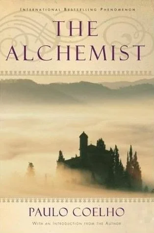 Book cover of "The Alchemist" by Paulo Coelho, featuring a misty landscape with a silhouette of a castle and cypress trees.