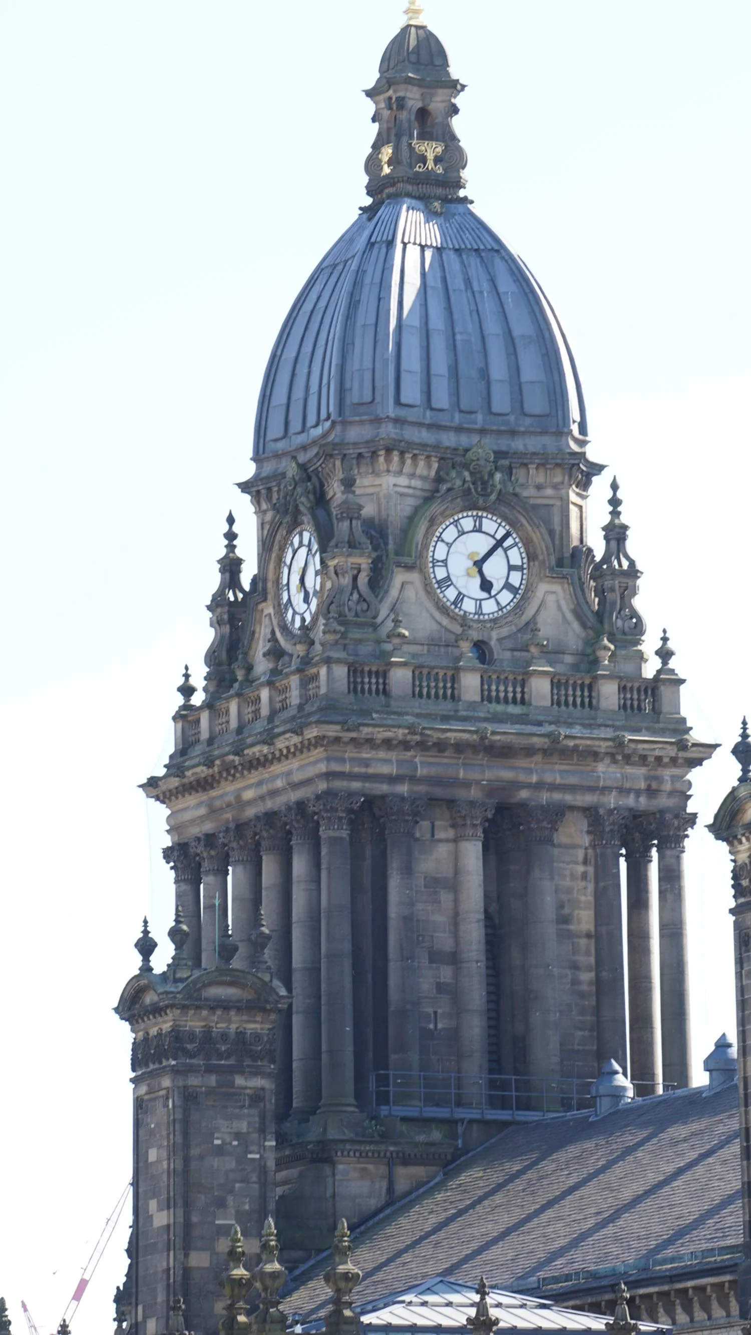 Close-up of a historic clock tower with a large statue at the top, gothic architectural details, and a metal-domed roof.