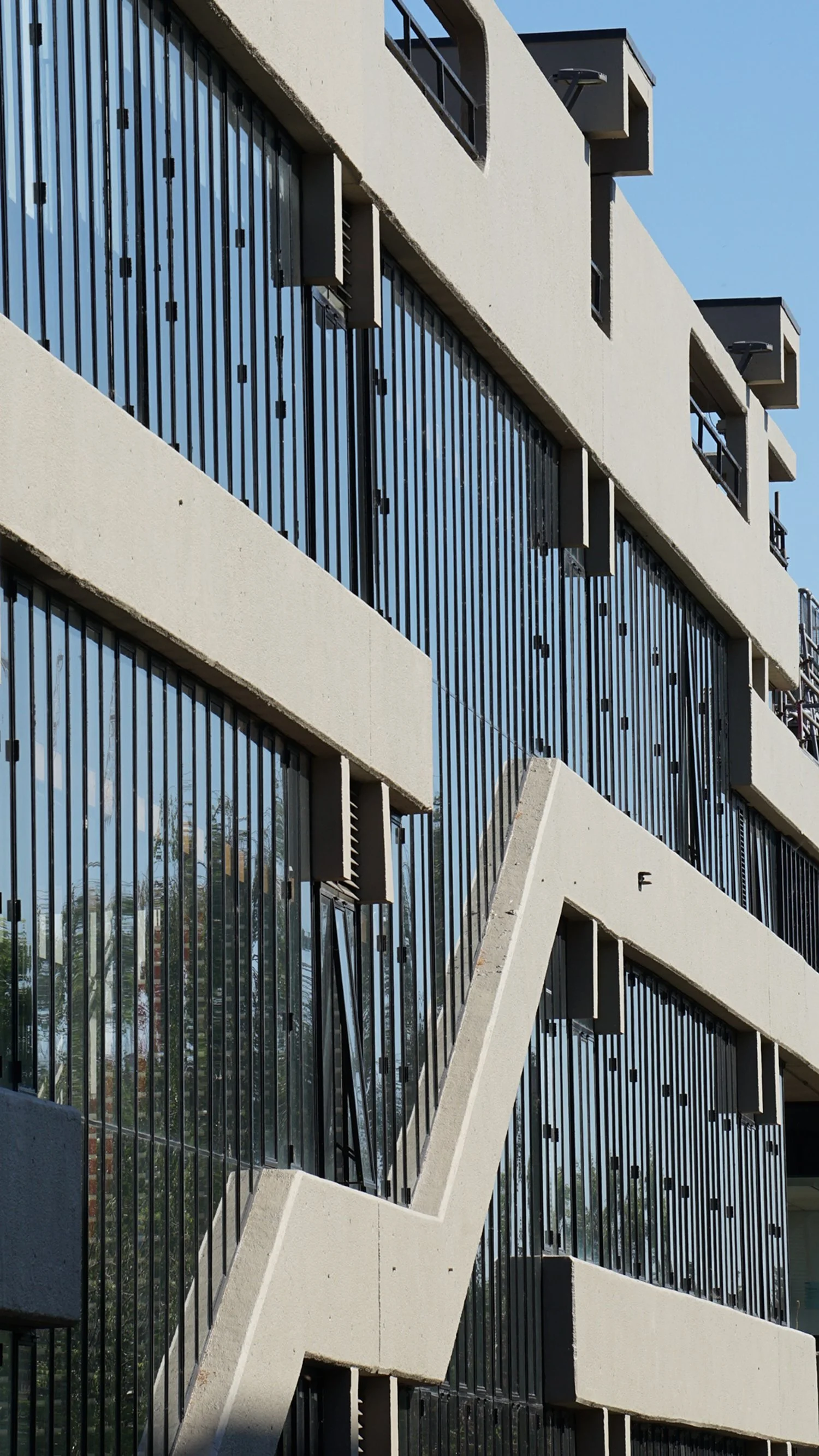 Modern building with concrete balconies and glass windows, featuring black metal bars for safety and an angular architectural design.