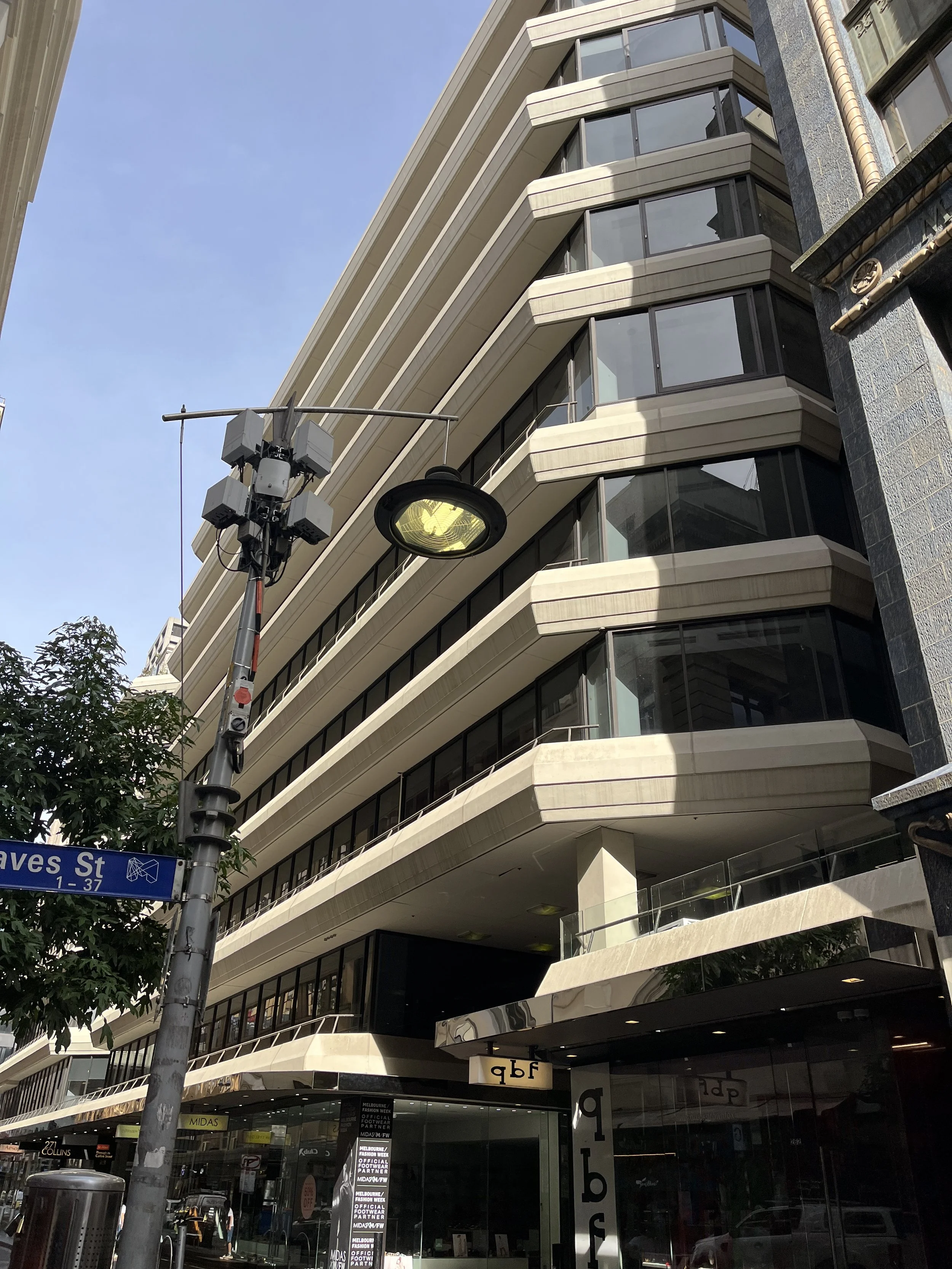 A modern multi-story building with curved balconies and glass windows on each floor, situated on a city street with a street lamp and street sign for Ives Street in front.