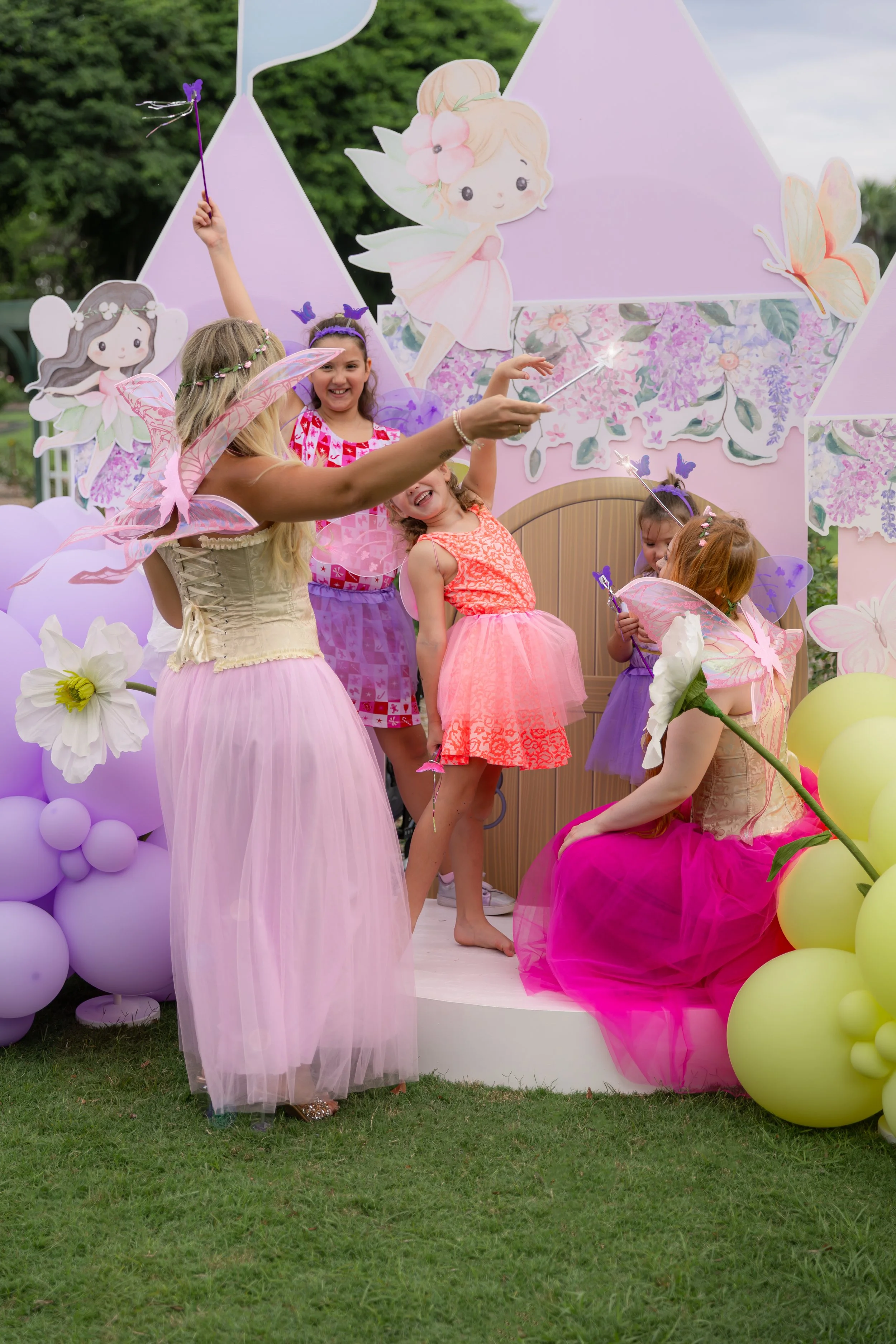 Children dressed in fairy and princess costumes celebrating at a fairy-themed party with balloons and fairy decorations.