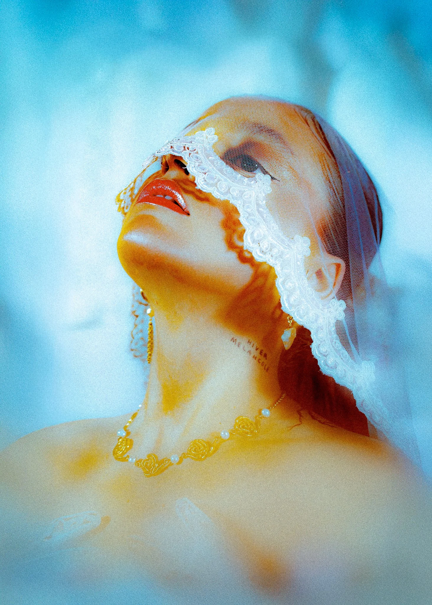 Mannequin portant une perruque et un maquillage sophistiqué, orné d'une voilette en dentelle blanche et d'une parure en perles et or, avec un tatouage sur le cou.