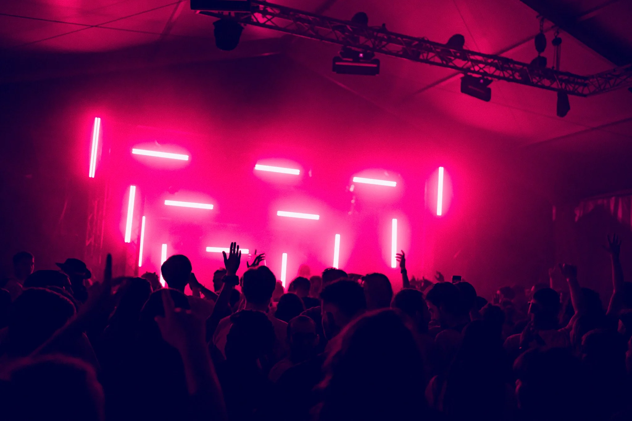 Une foule de personnes dansant lors d'un concert ou festival avec des lumières roses et violettes fluo
