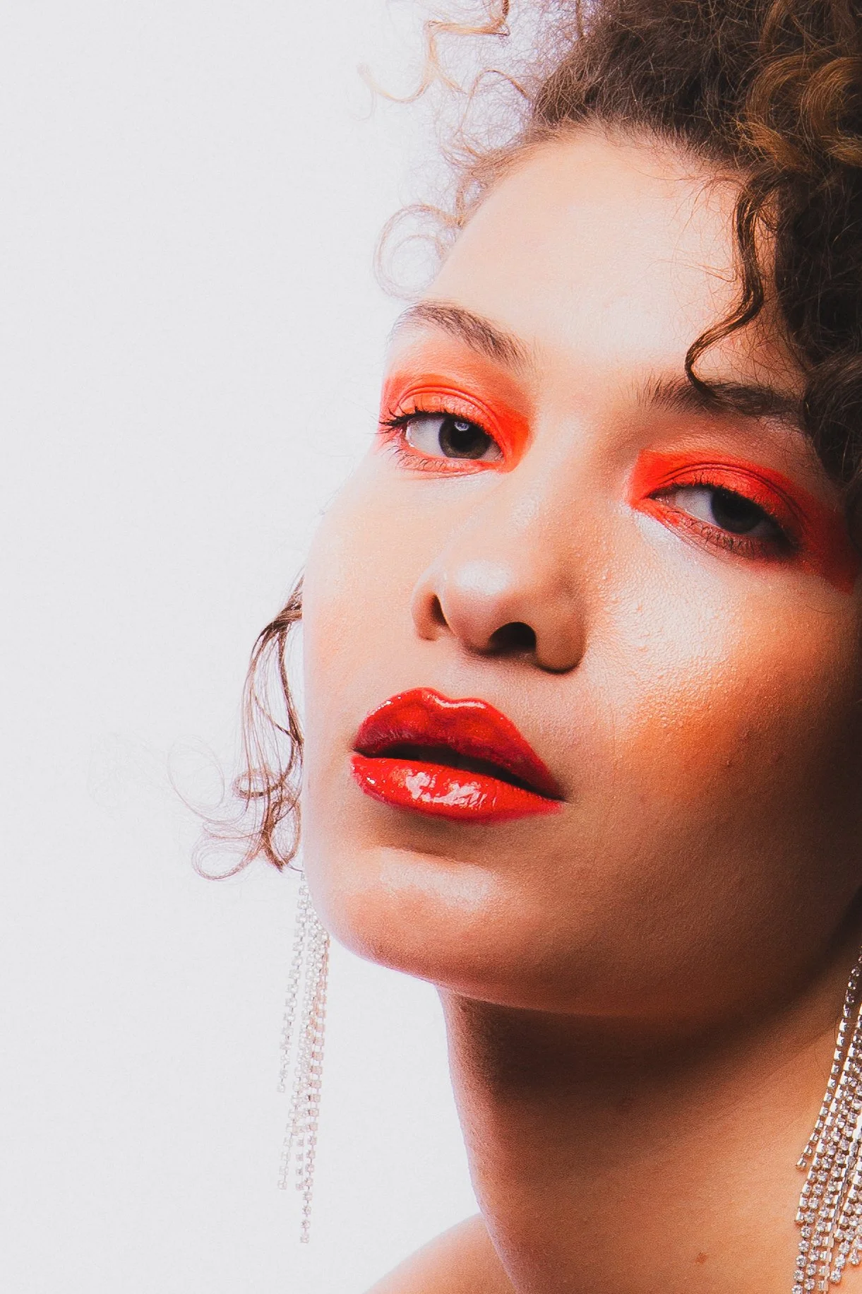 Portrait d'une femme avec maquillage rouge vif sur les yeux et les lèvres, portant des boucles d'oreilles pendantes avec des chaînes de diamants.