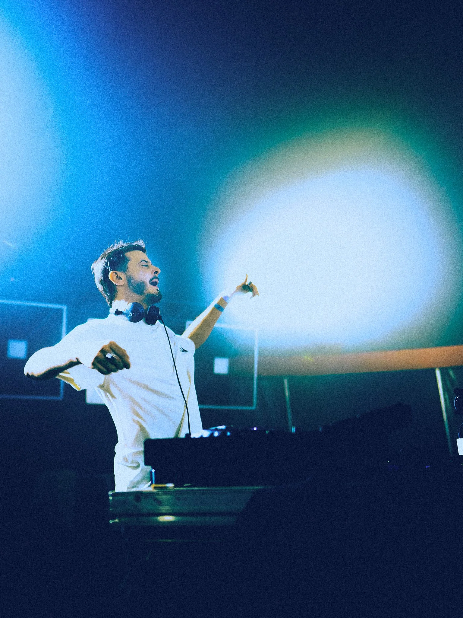 DJ jouant de la musique dans un club, avec des lumières colorées et un casque autour du cou.