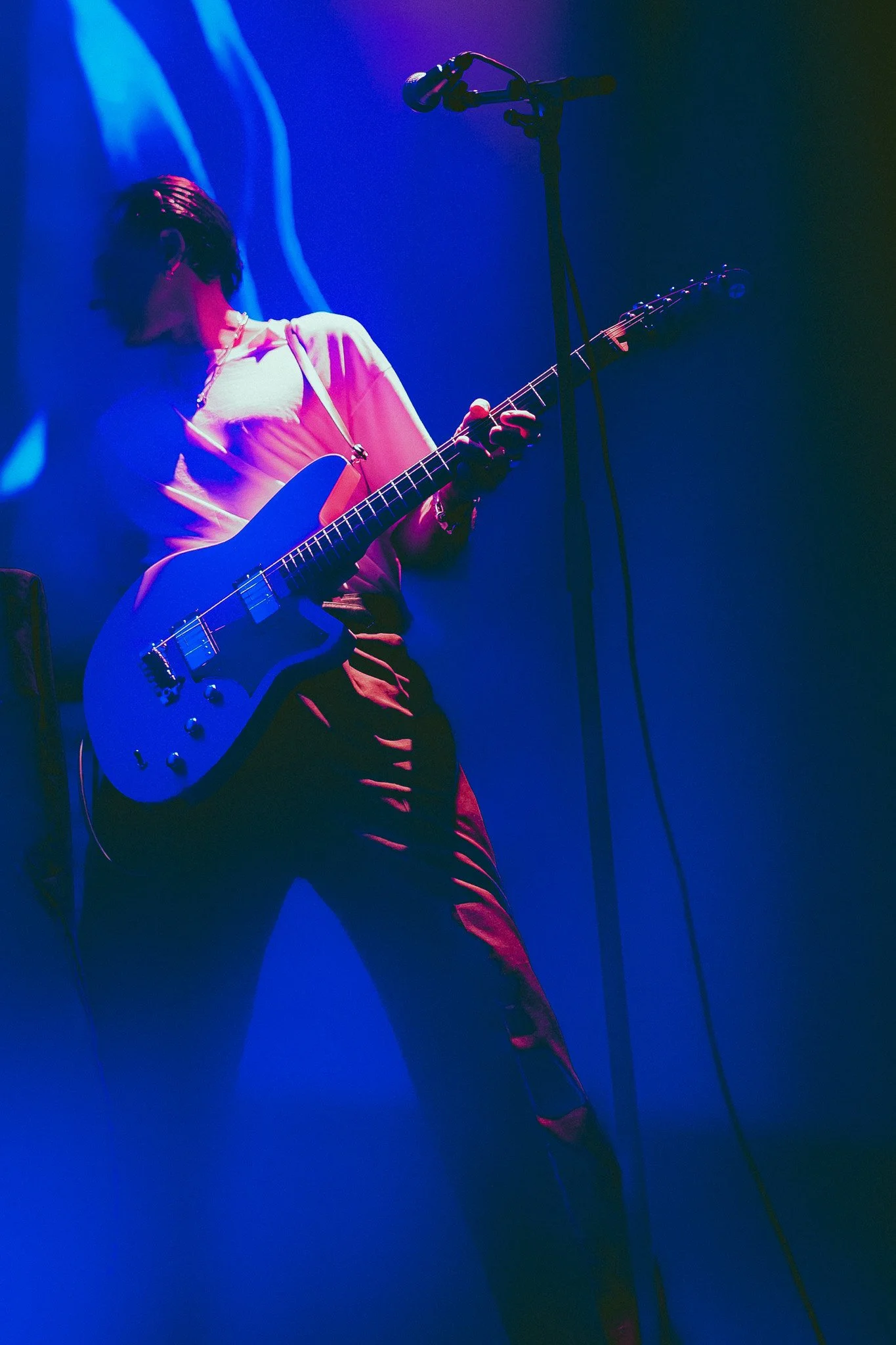 Musicienne jouant de la guitare lors d'une performance sur scène avec un éclairage violet et bleu.