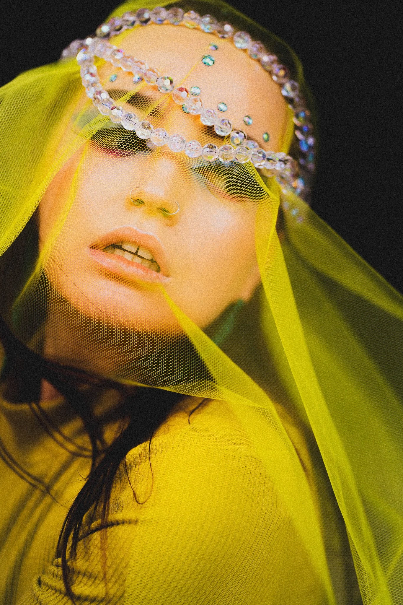 Femme aux yeux maquillés portant un voile en tulle jaune, avec un bandeau de bijoux en cristaux sur le front, fond noir