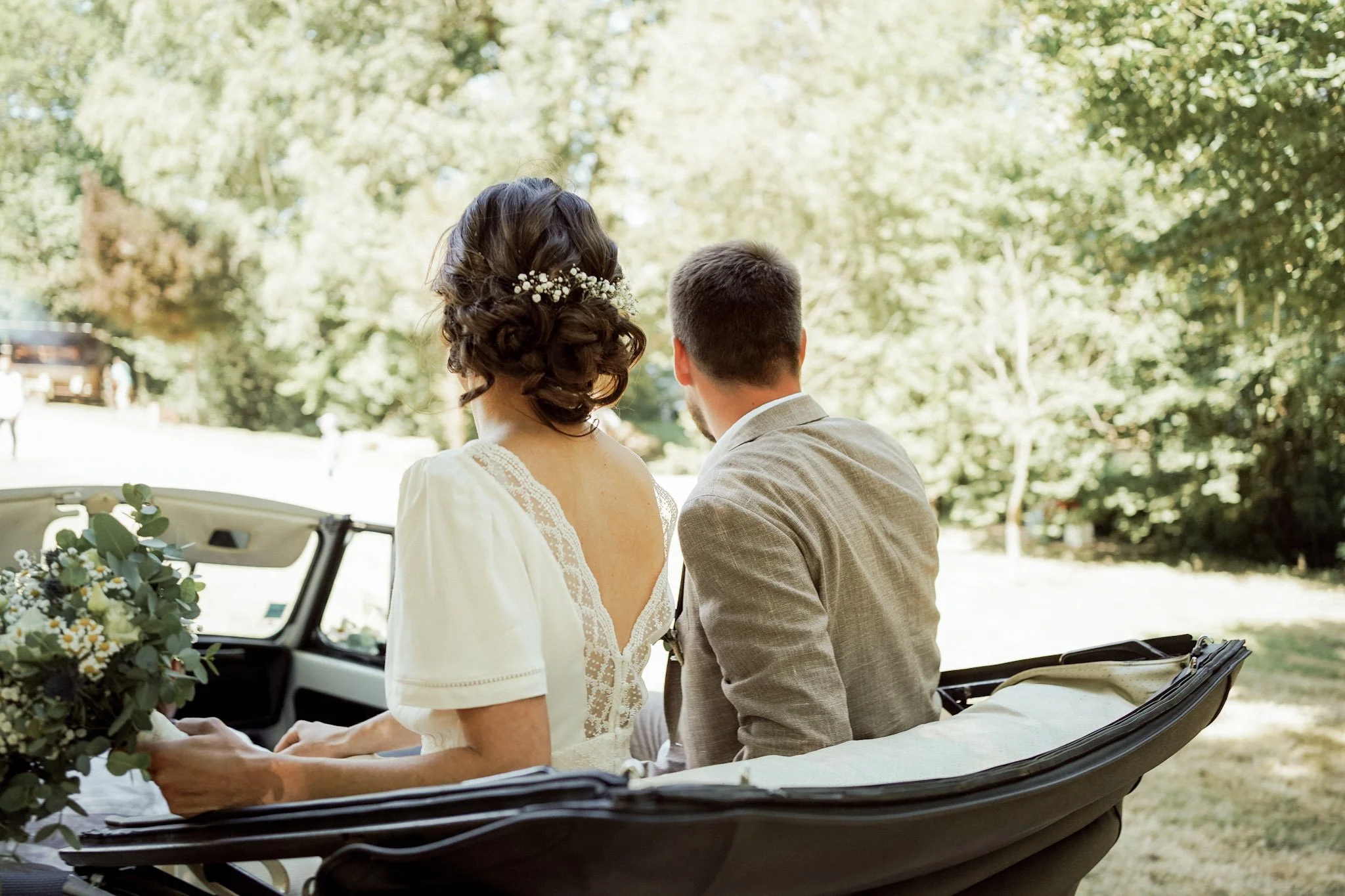 Un couple assis dans une voiture électrique lors d'une cérémonie en extérieur, entouré d'arbres et de végétation.