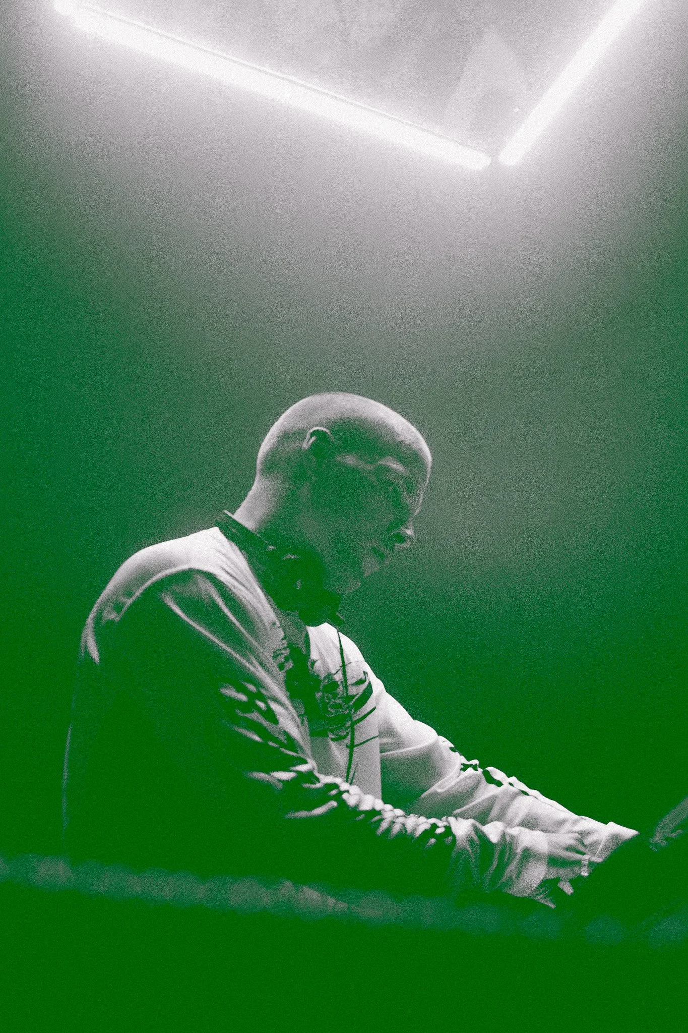 Un DJ souriant joue de la musique à l'aide d'un équipement DJ dans une pièce sombre, éclairée par un plafond lumineux.