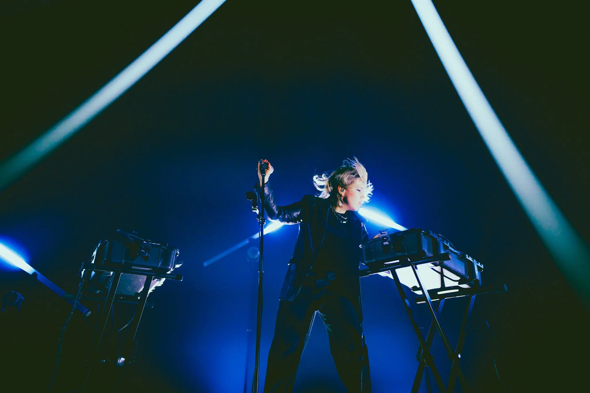 Une femme performe sur scène avec des appareils électroniques, éclairée par des lumières bleues et vertes.