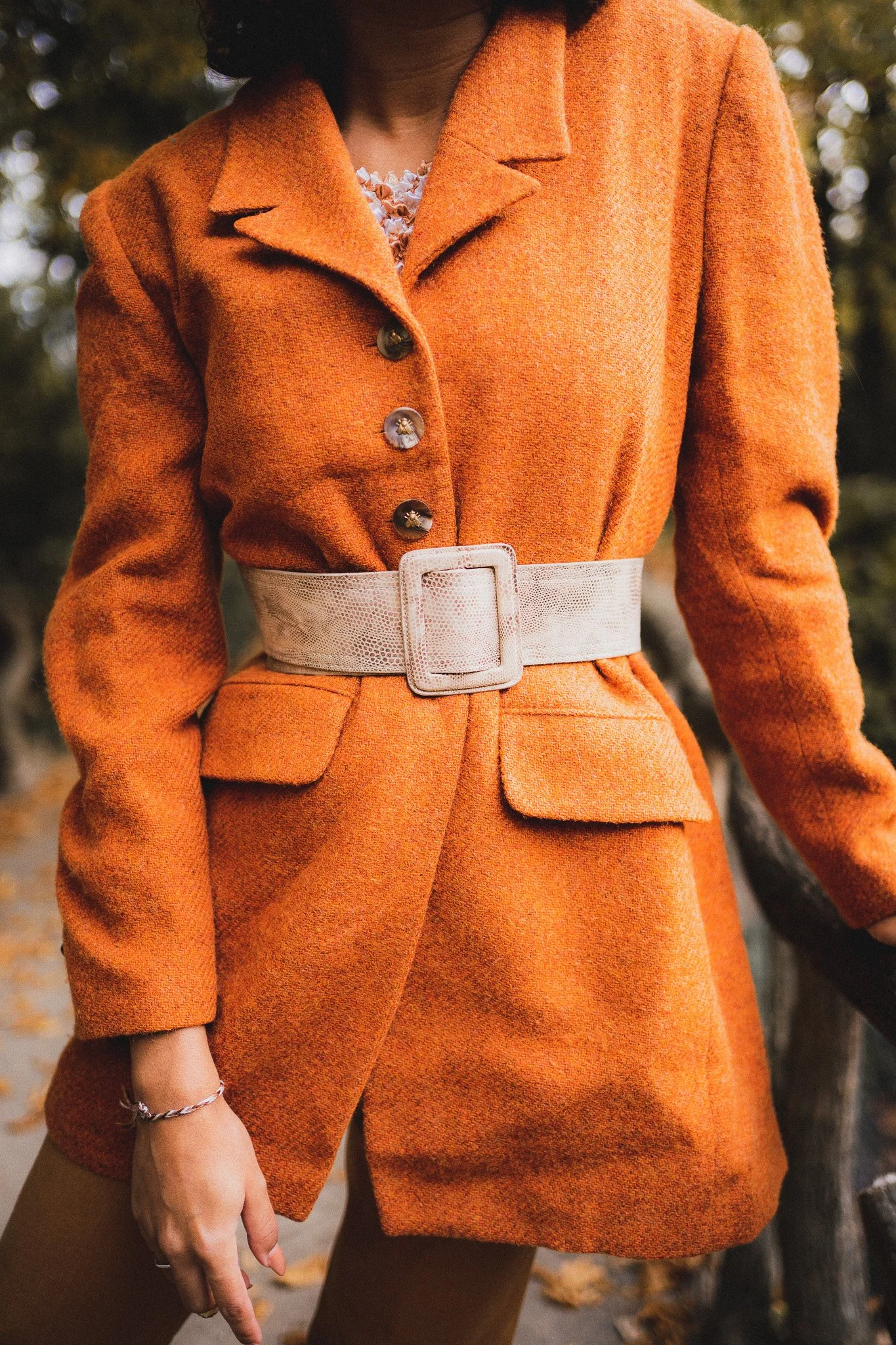Femme portant un manteau orange avec une ceinture beige en extérieur.