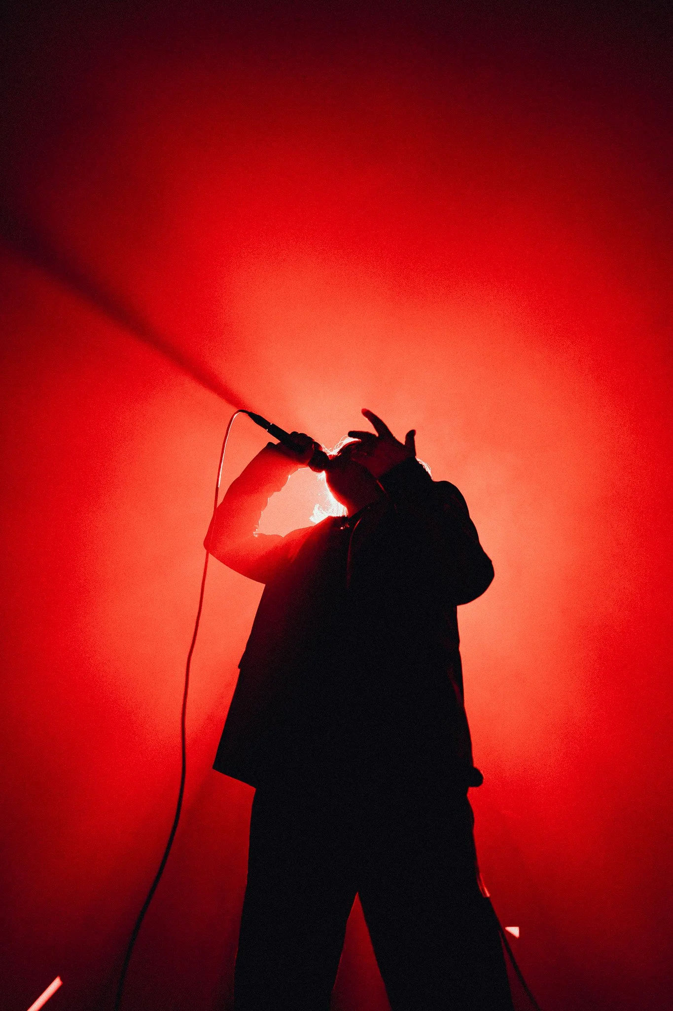 Silhouette d'un chanteur ou musicien avec un micro, éclairé par une lumière rouge intense.