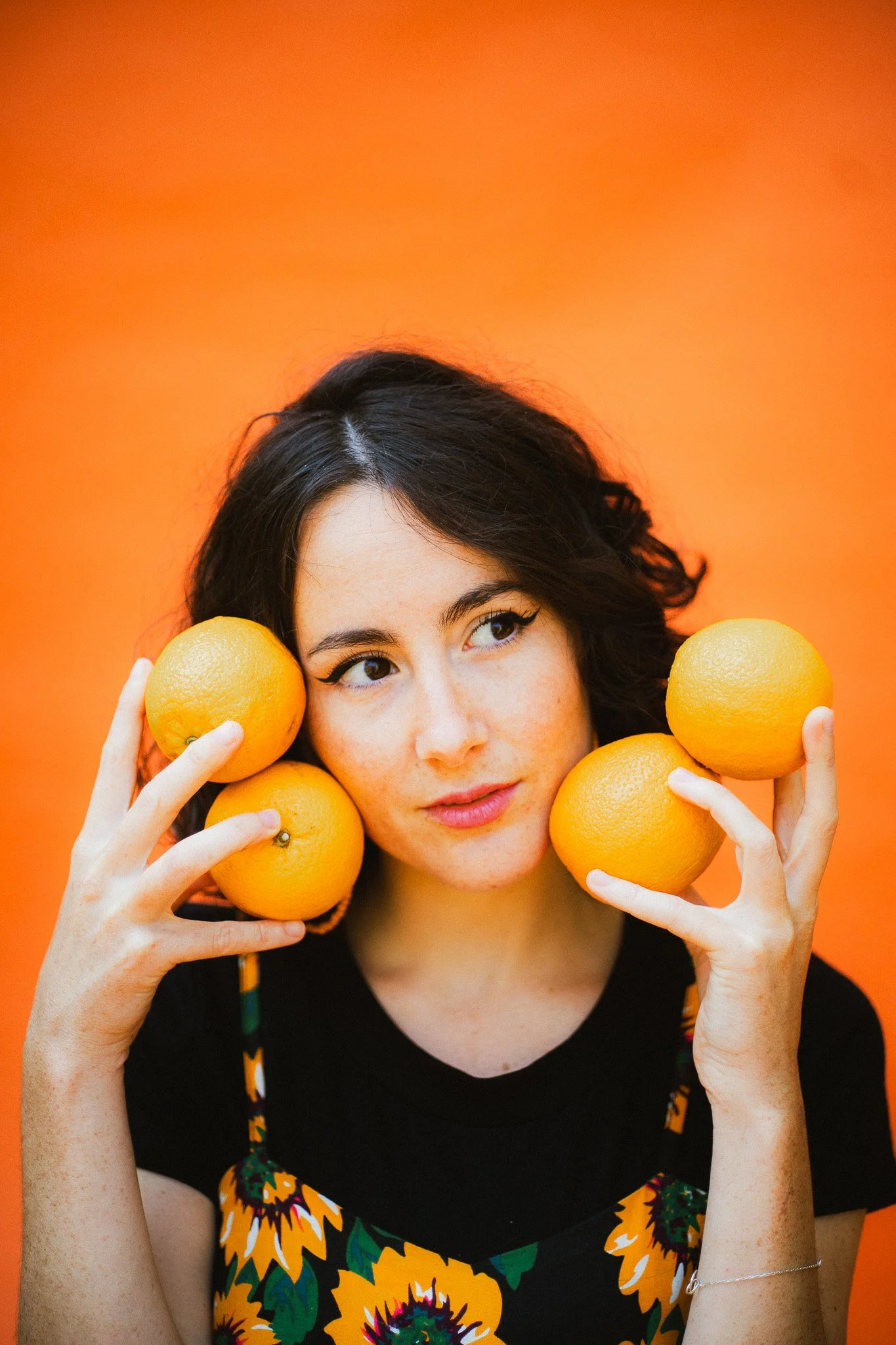 Femme avec des oranges, portant une robe à motif tournesol, contre un fond orange.