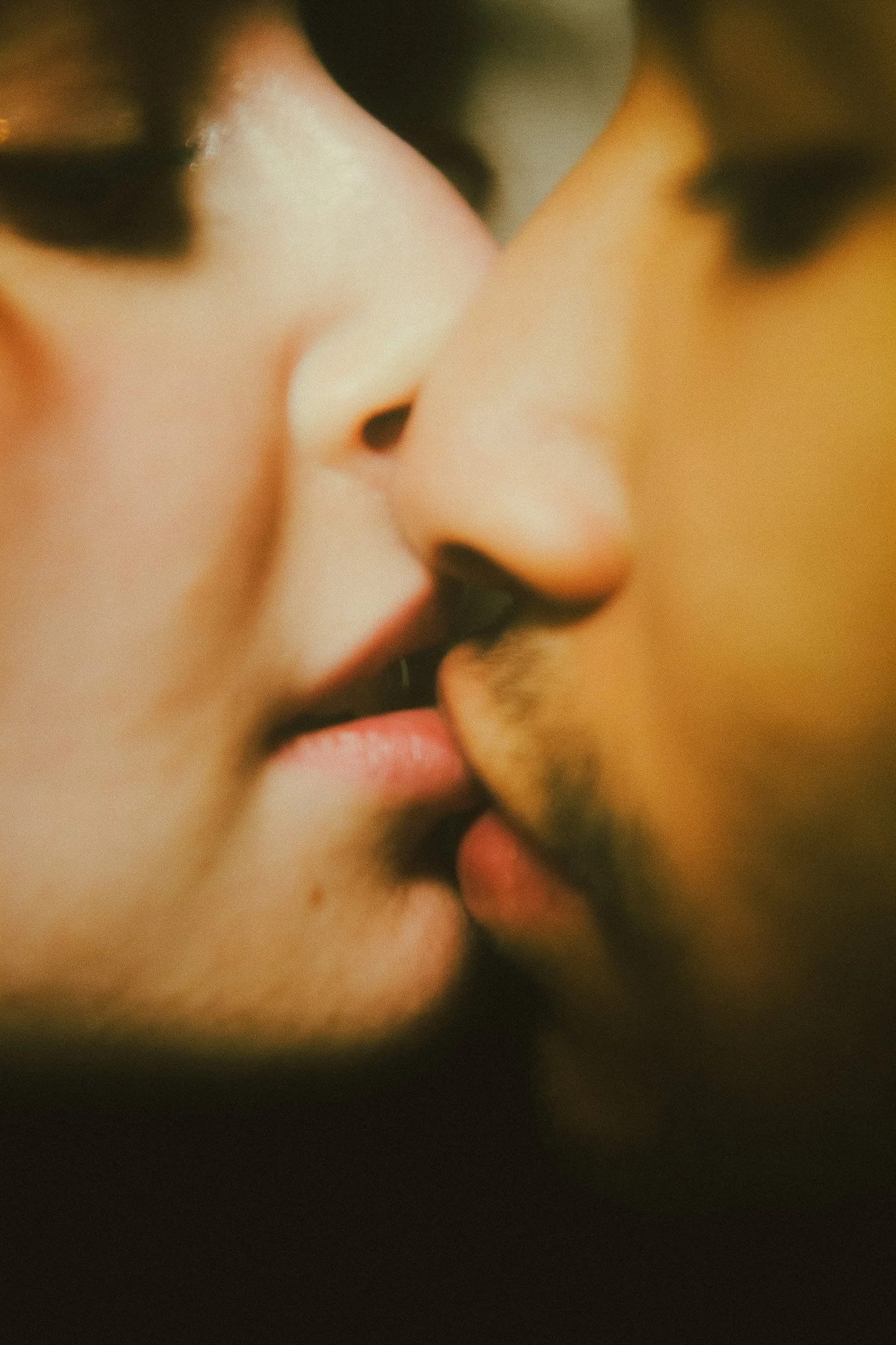 Close-up d'un couple qui s'embrasse, montrant leur nez, lèvres et partie du visage, avec un fond flou.