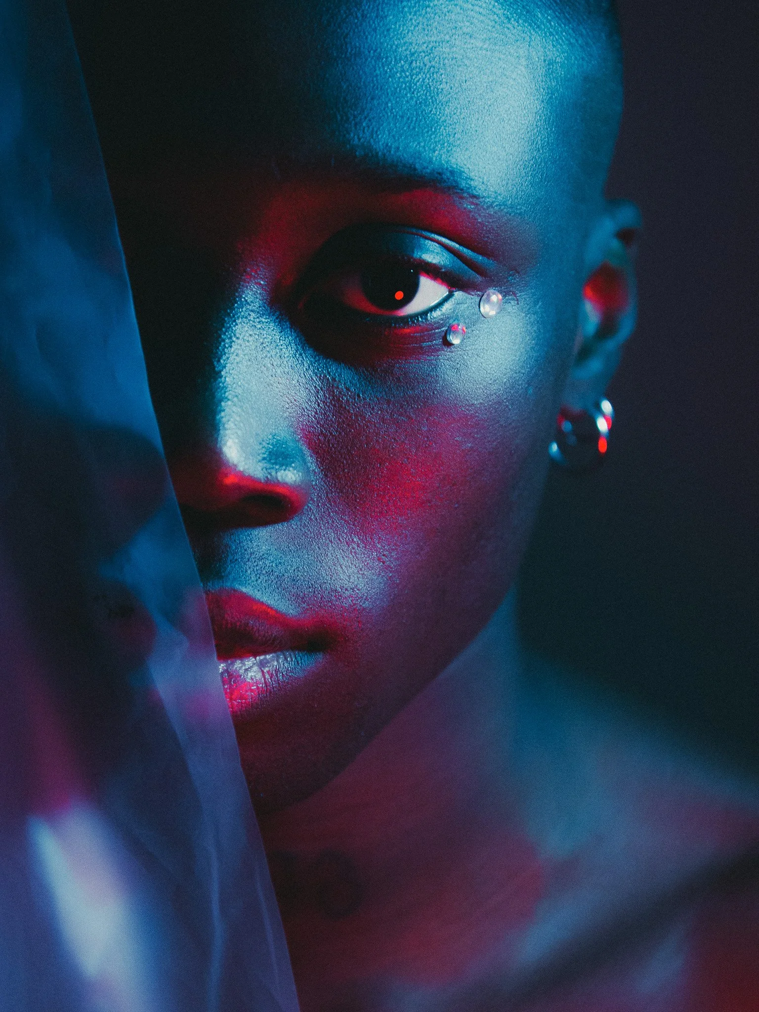Portrait d'une femme avec maquillage coloré, regard intense, éclats de lumière bleue et rouge, portait artistique, style moderne et urbain.