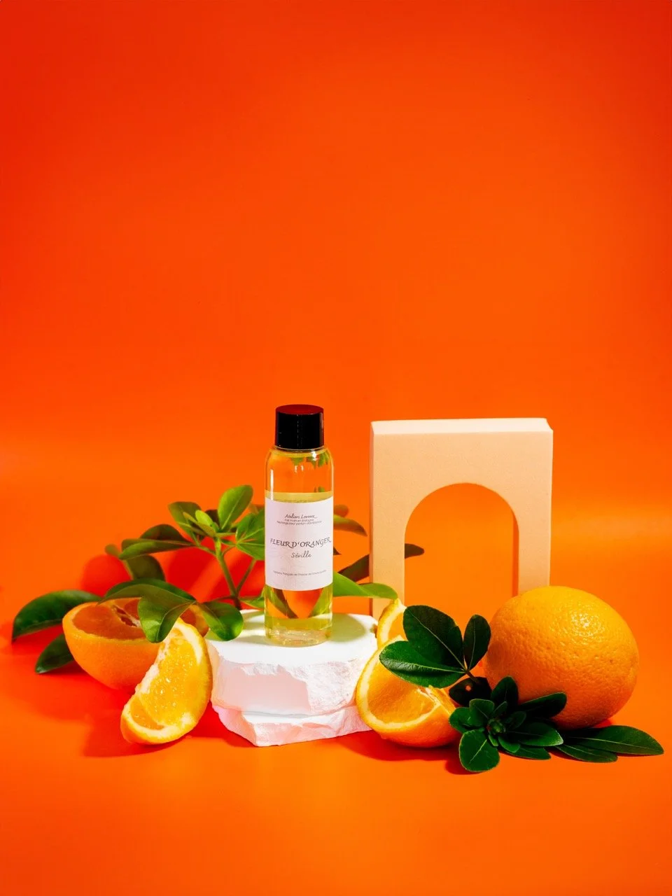 Une bouteille de parfum avec des segments d'orange, un citron, des feuilles vertes, un fond orange