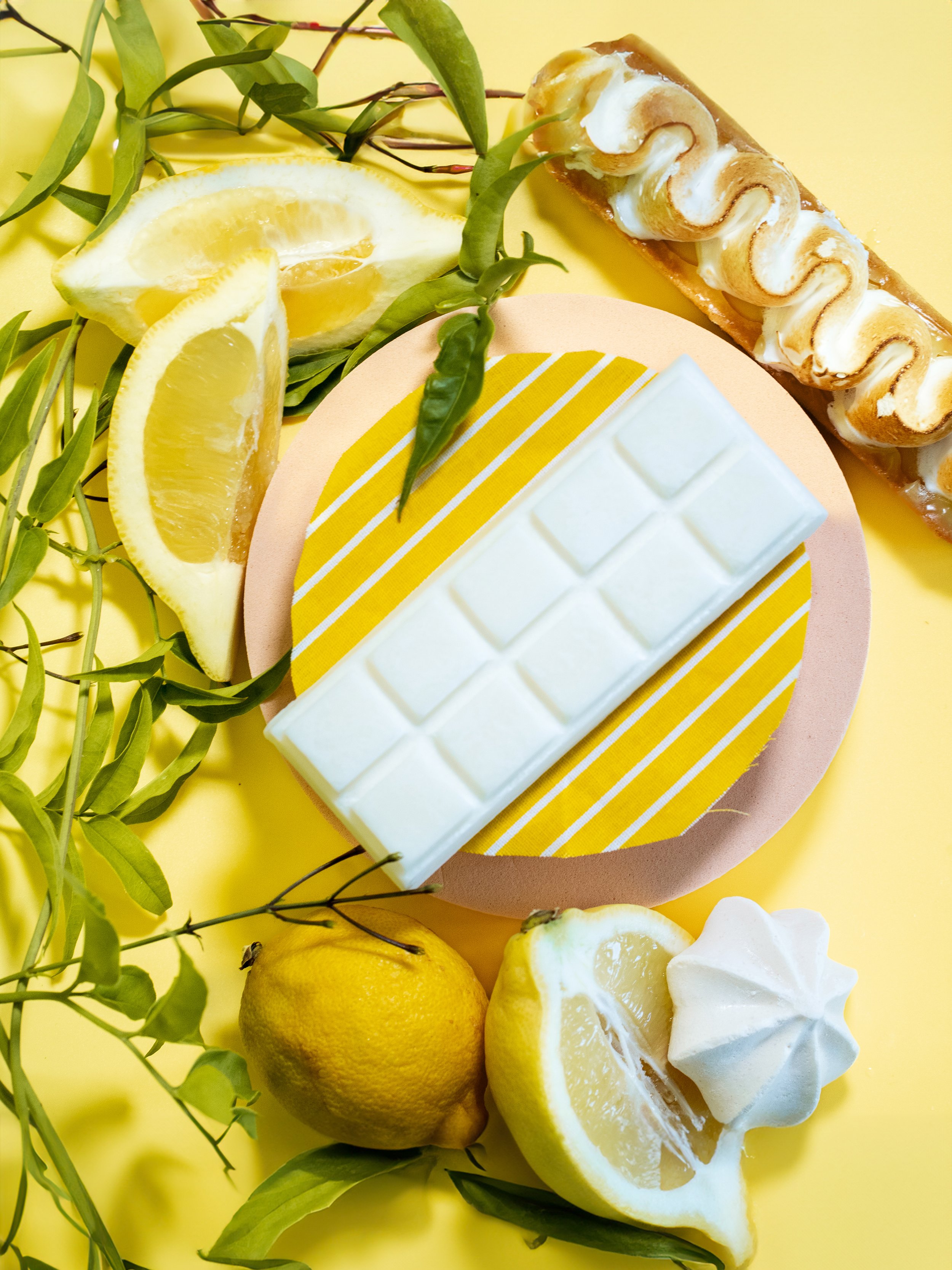 Morceaux de citron, une barre de chocolat blanc, un gâteau à la crème, et une pâte à gâteau décorée avec des rayures jaunes, avec des feuilles vertes
