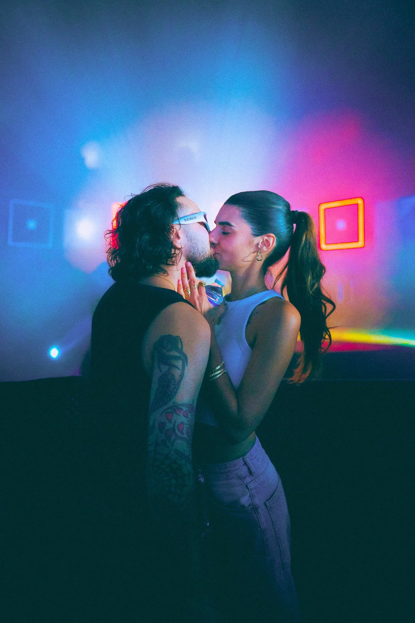 Un couple s'embrasse dans une ambiance de fête avec des lumières colorées.