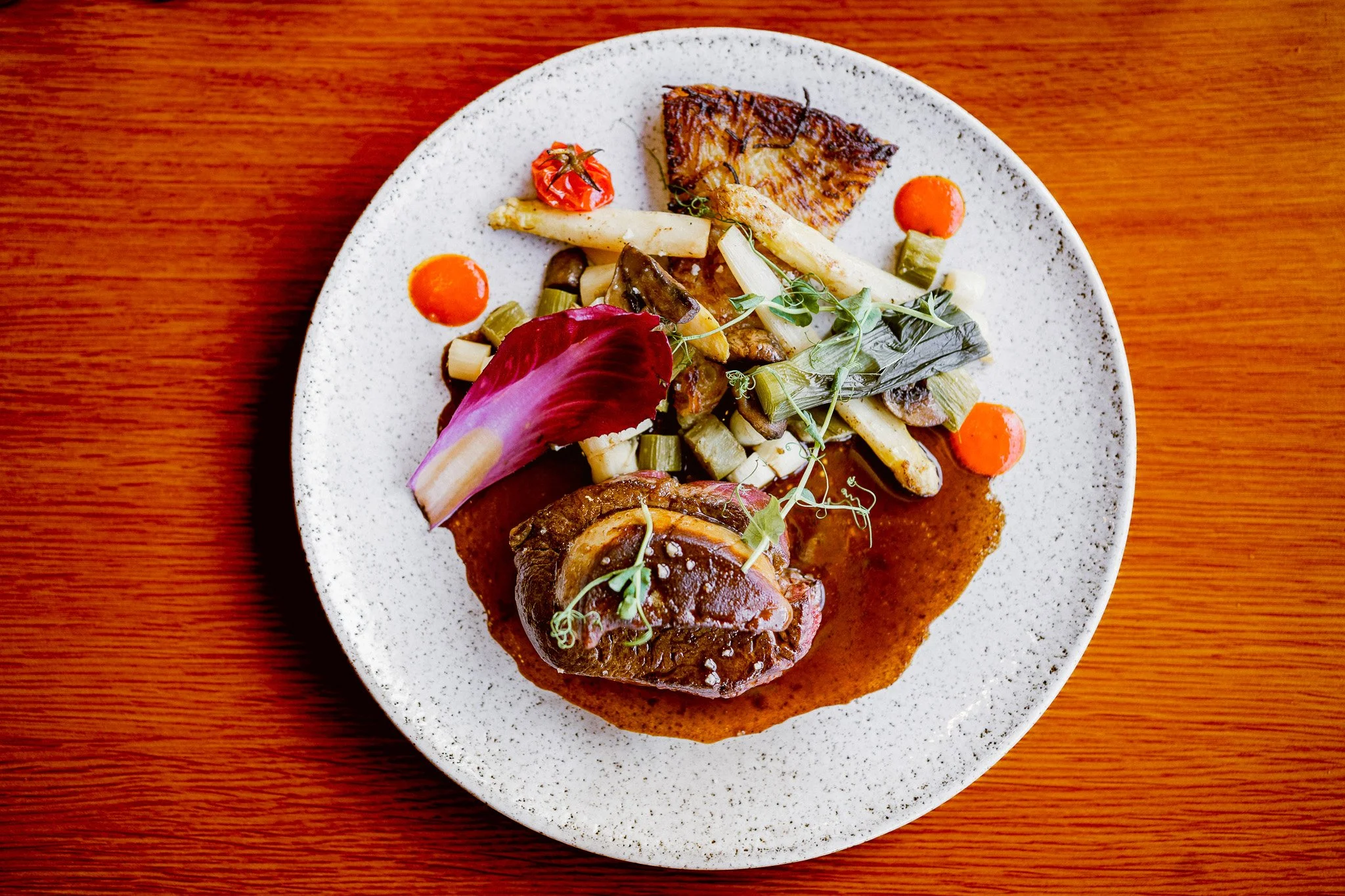 Assiette de viande avec sauce, accompagnée de légumes variés dont carottes, céleri, champignons, et garnie de microgreens sur une table en bois.