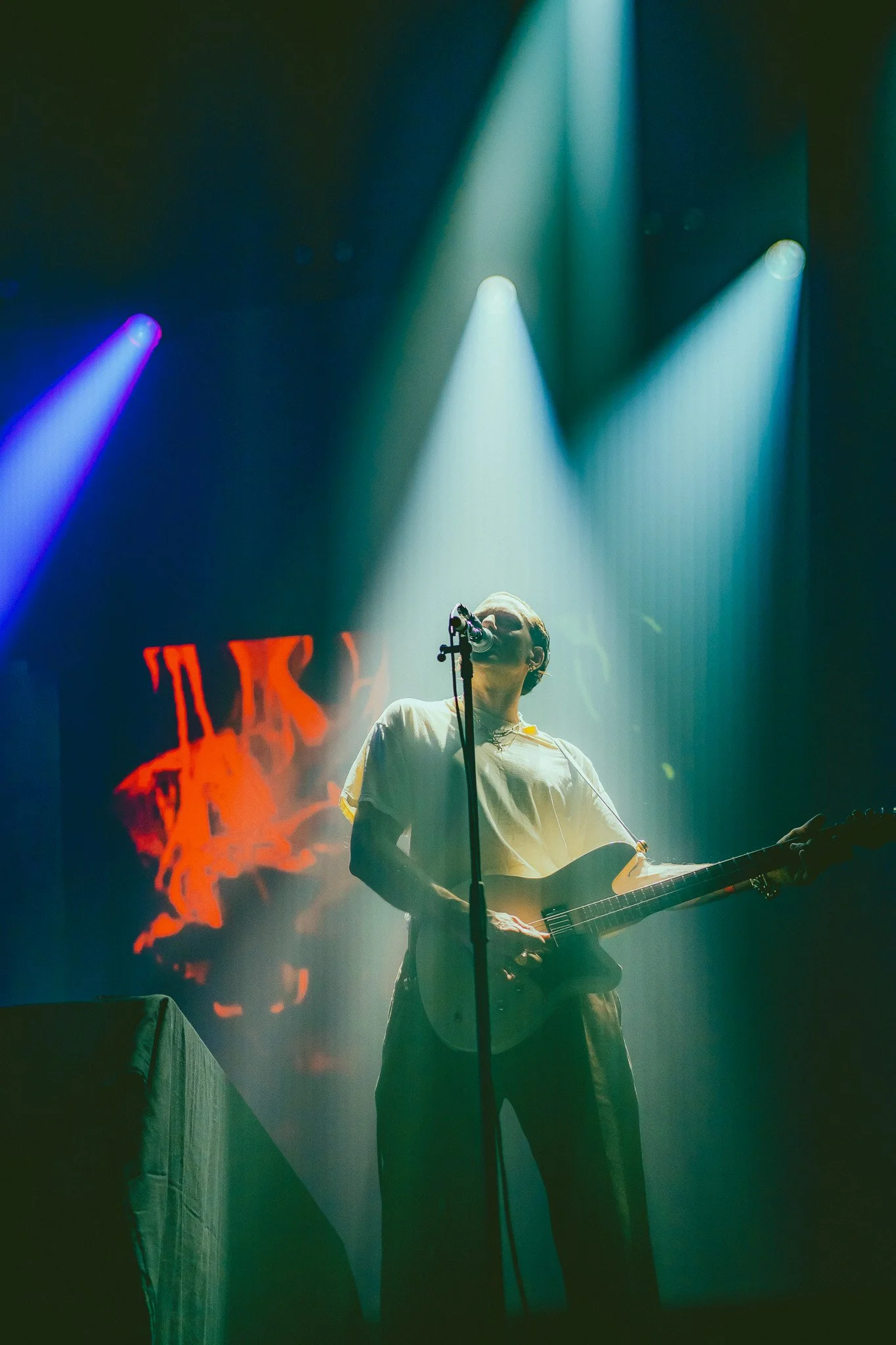 Musicien jouant de la guitare sur scène avec un éclairage vibrant et un écran lumineux en arrière-plan.