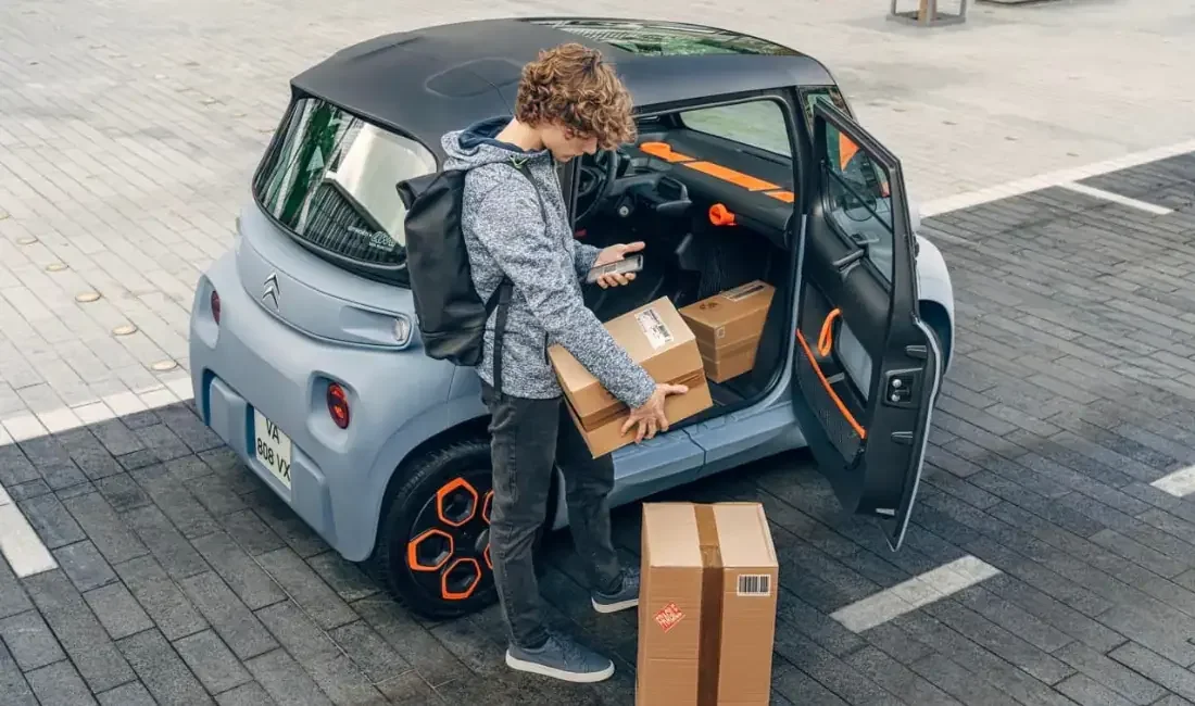 Jeune homme déchargeant des cartons dans une petite voiture électrique en stationnement