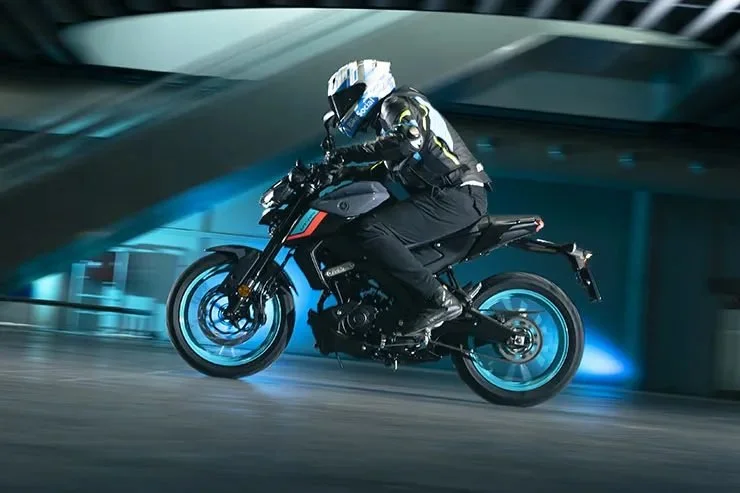 Un motard portant un casque et une veste de sécurité, roulant rapidement à moto dans un environnement urbain la nuit, avec des effets de lumière bleue