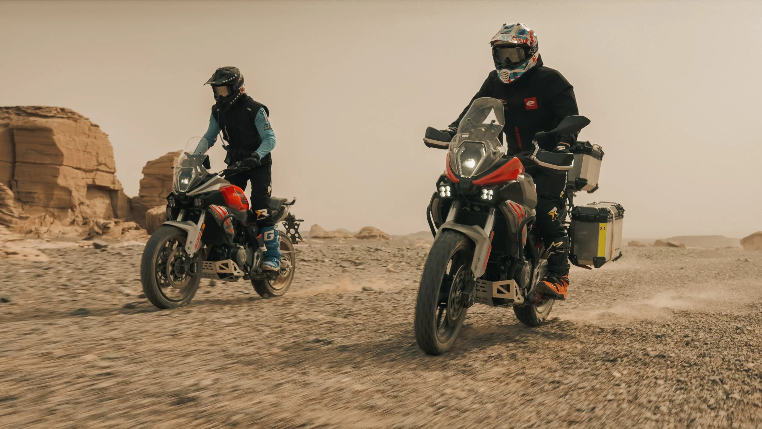 Deux motards traversant un paysage désertique rocheux sous un ciel clair.