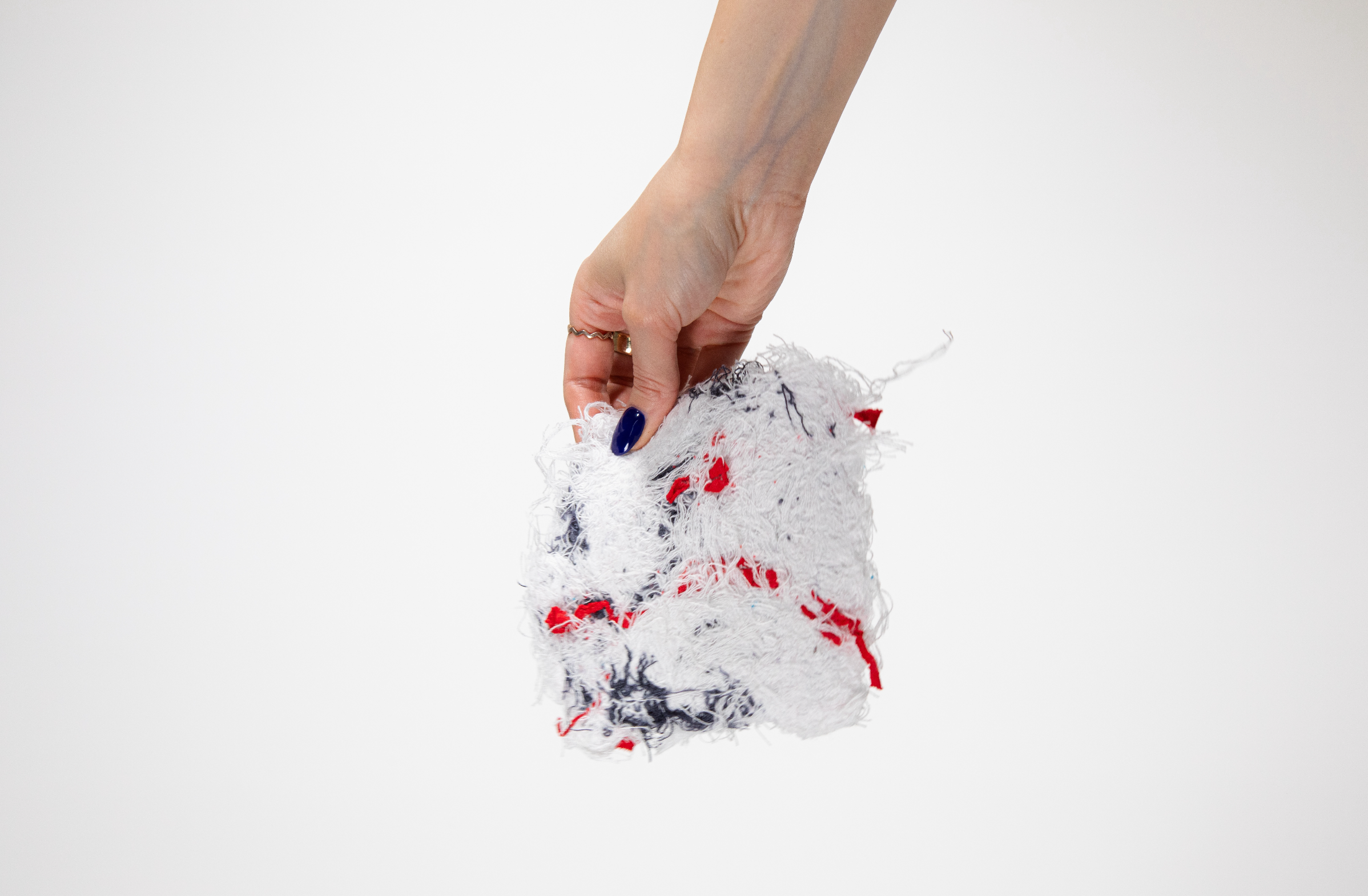 Hand holding a soaked, crumpled white cleaning scrub pad with red and blue accents, against a plain white background.