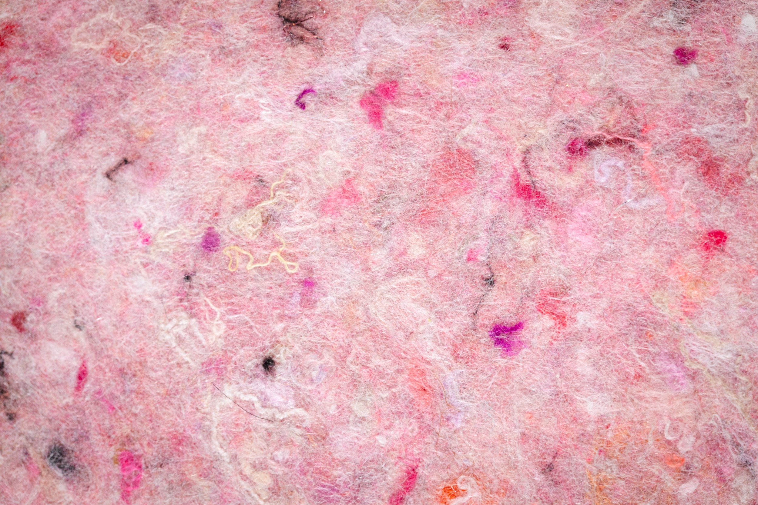 Close-up photo of a pink textured surface with various small colorful fibers, particles, and fuzz.