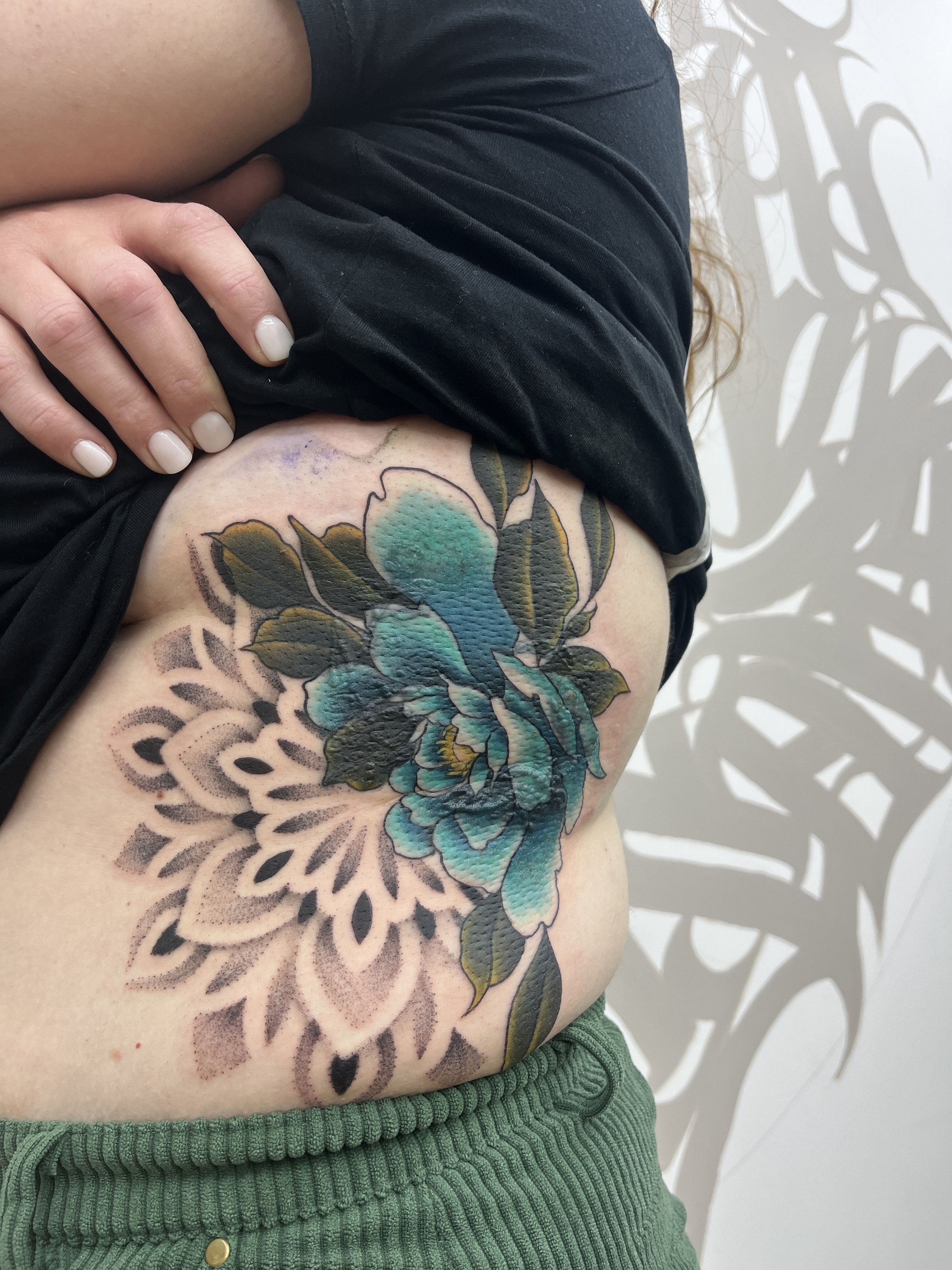 Tatouage de recouvrement sur les côtes avec pivoine turquoise et mandala géométrique en dotwork.