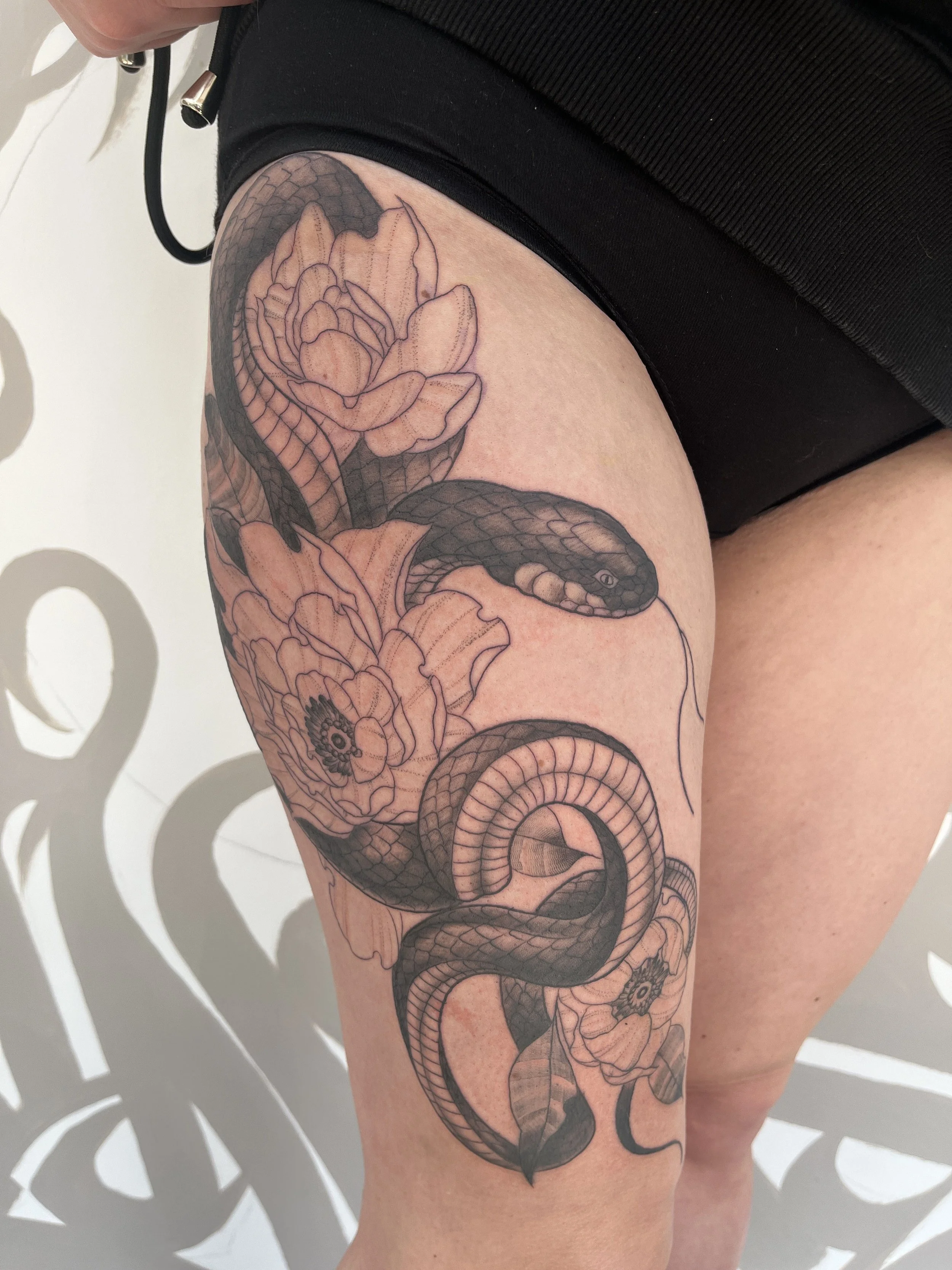 Tatouage blackwork représentant un serpent entouré de pivoines florales sur la jambe.