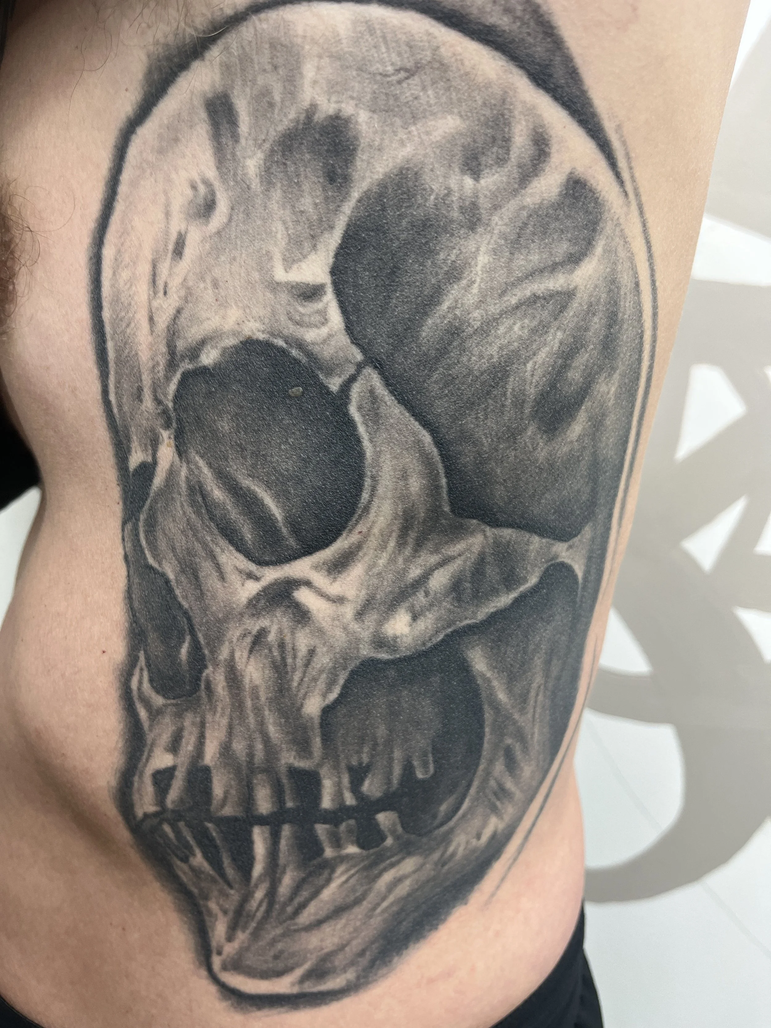 Tatouage réaliste de crâne humain réalisé en noir et gris sur les côtes.