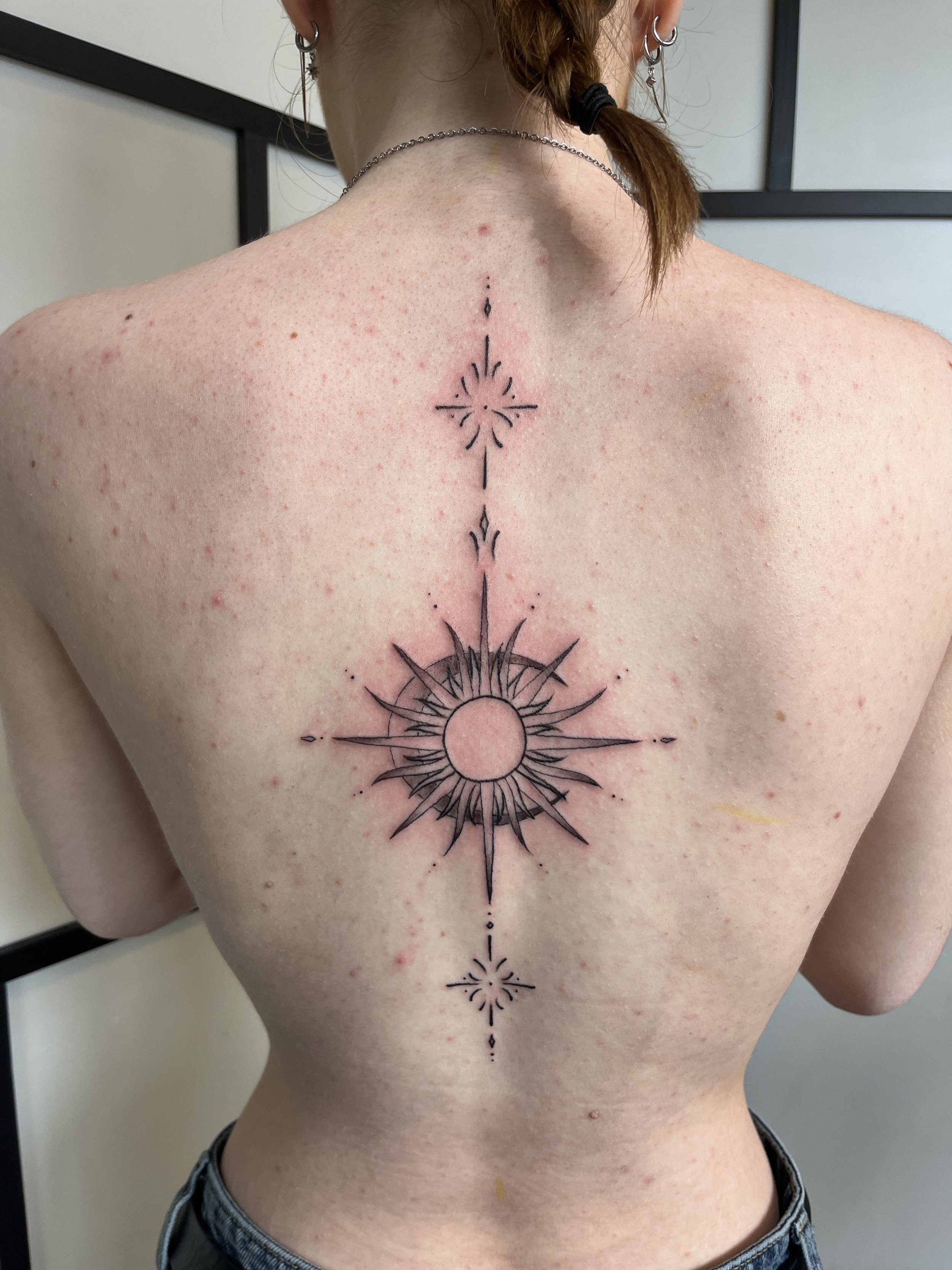 Tatouage ornemental géométrique dans le dos avec soleil central et lignes fines symétriques.