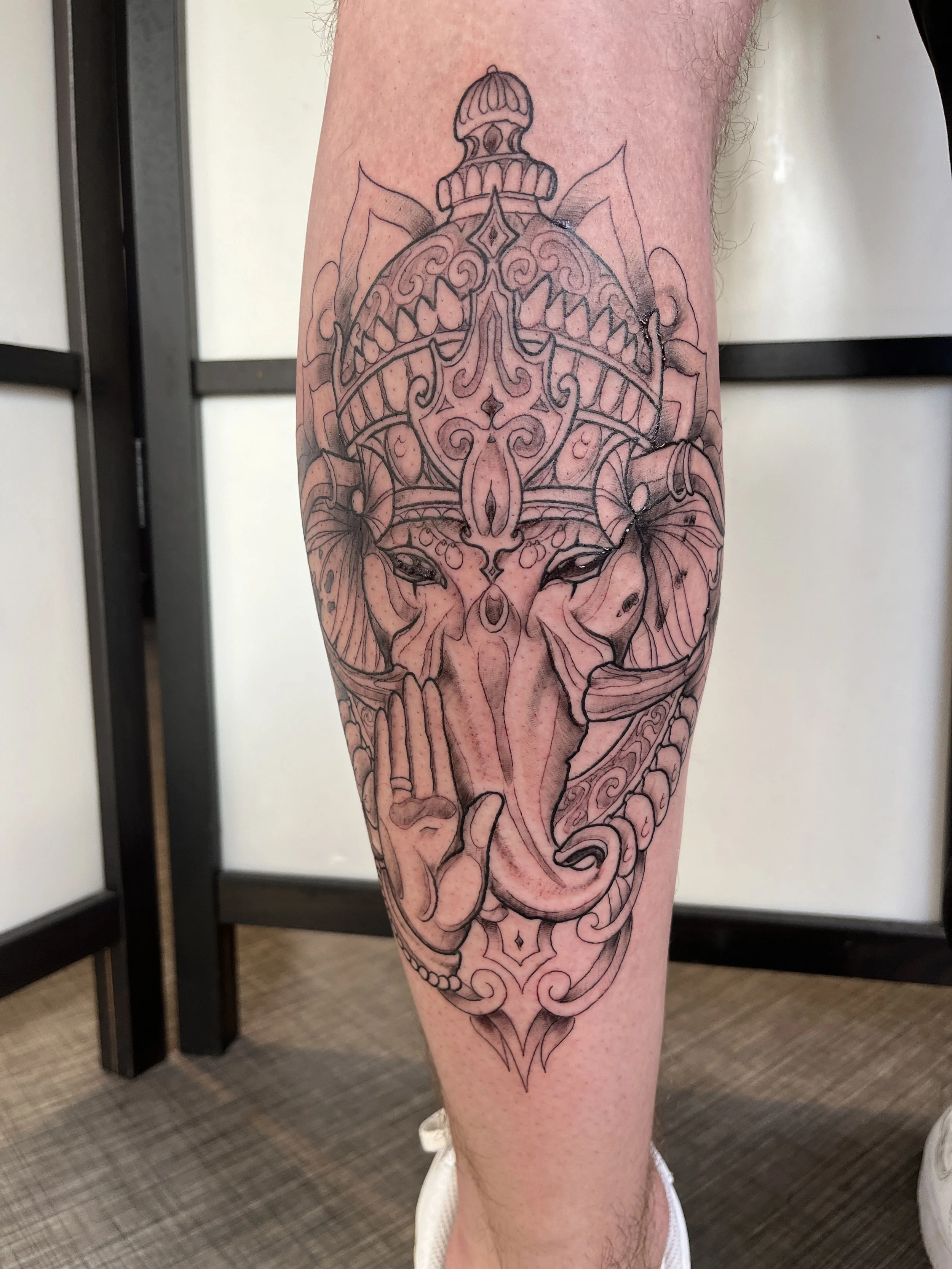 Tatouage blackwork représentant Ganesh avec motifs ornementaux sur la jambe.