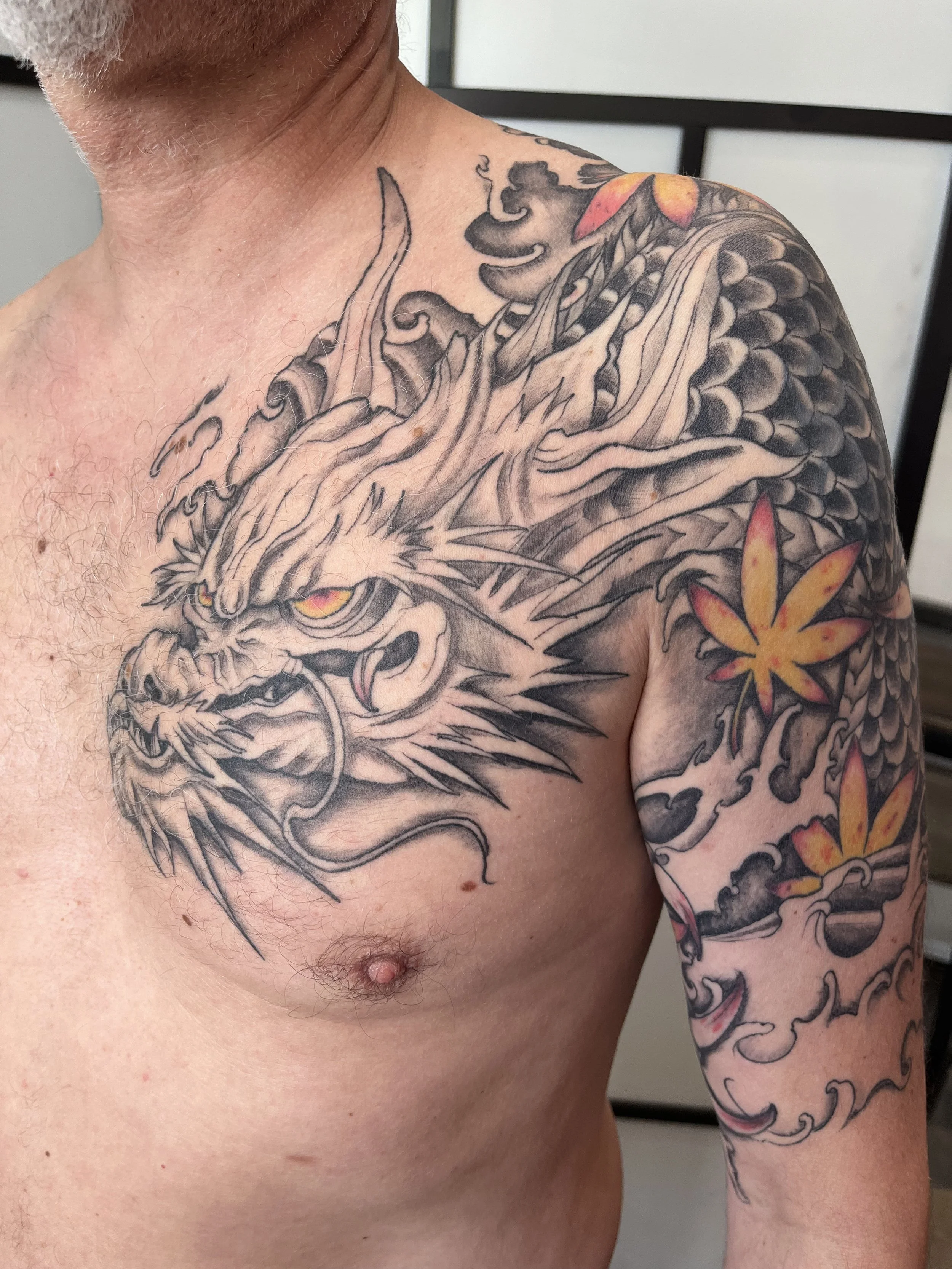 Tatouage japonais représentant un dragon avec vagues et fleurs réalisé en recouvrement sur le bras et le torse.
