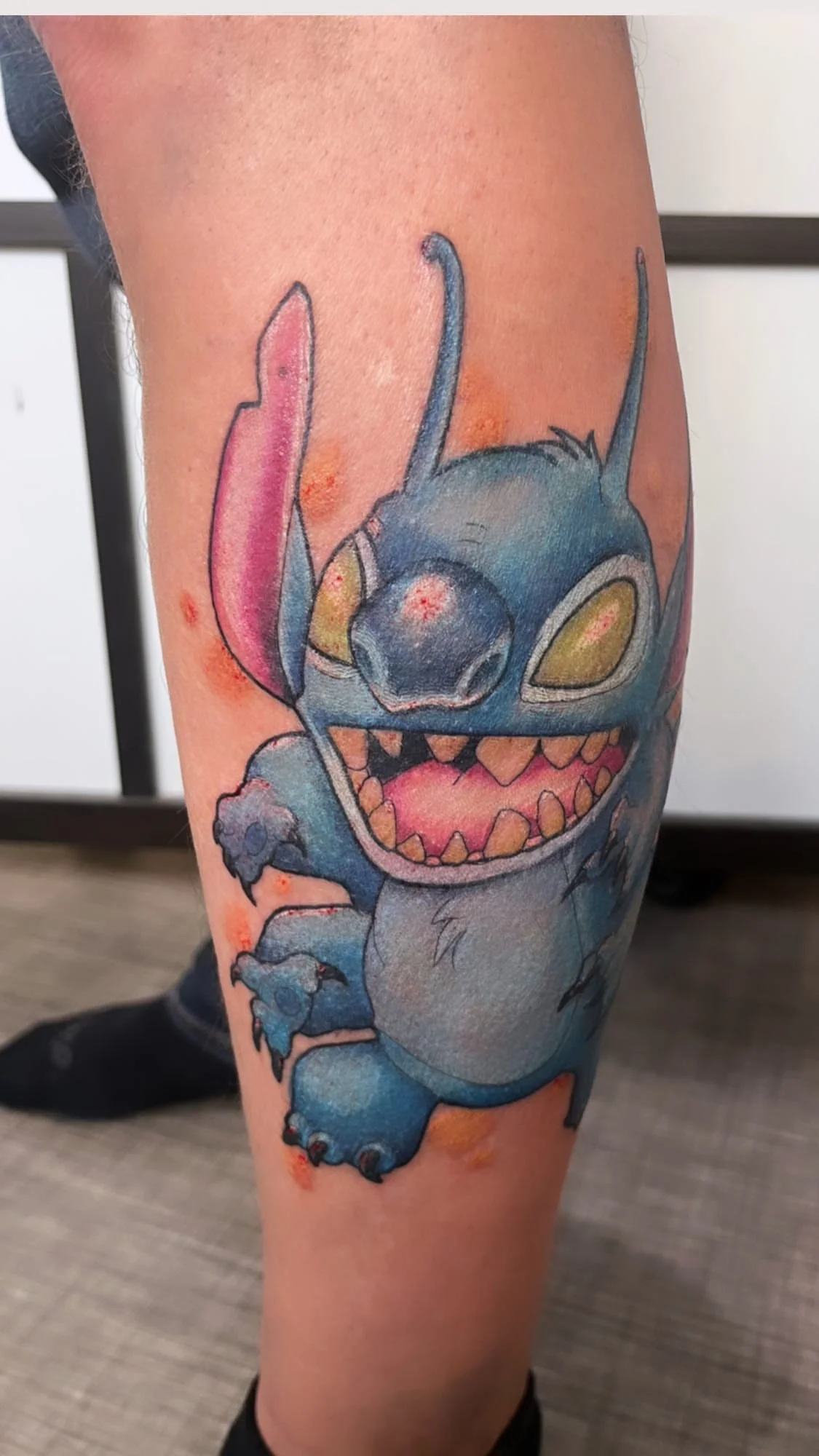 Tatouage cartoon coloré représentant Stitch sur la jambe.