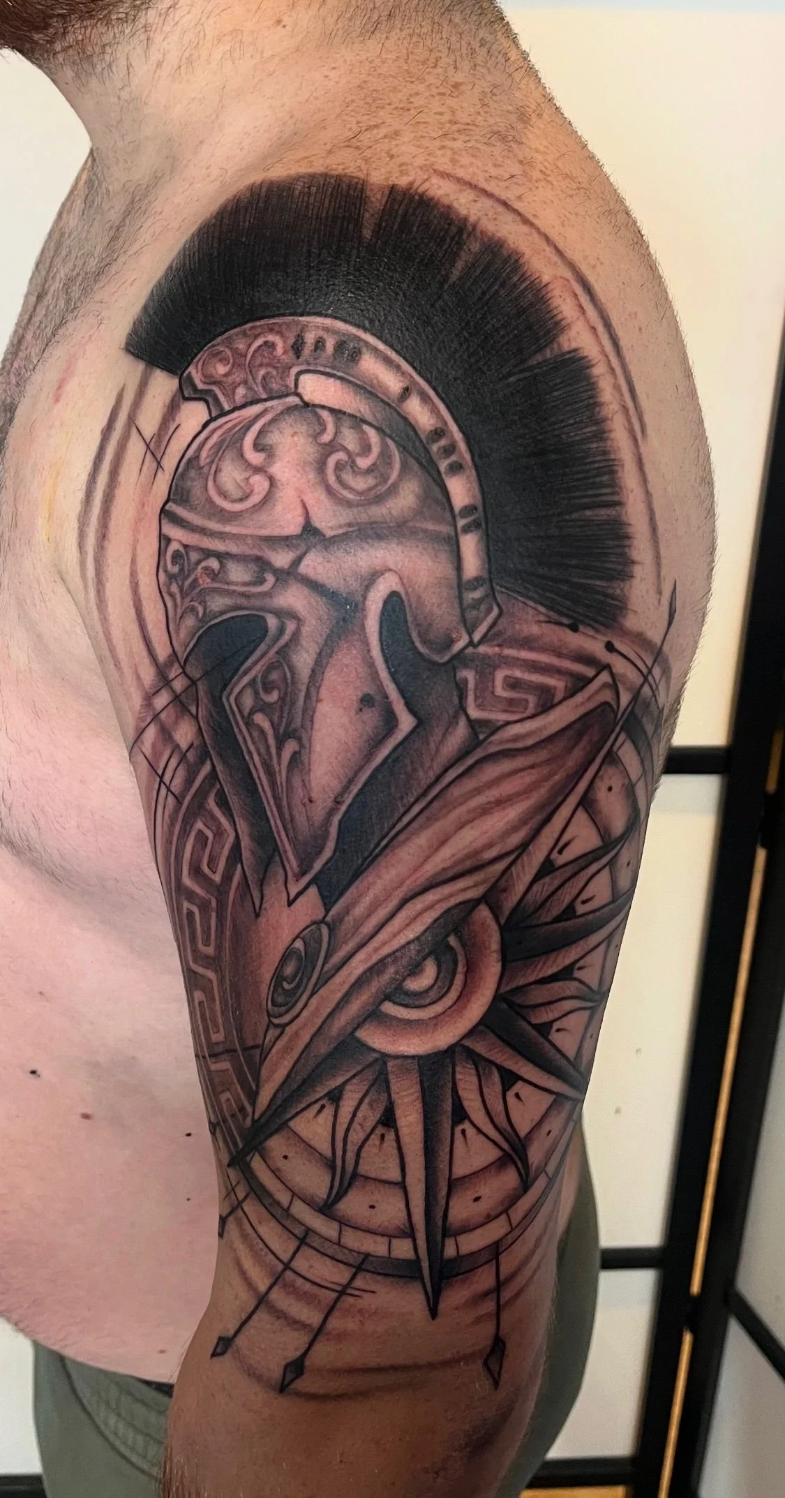Tatouage graphique représentant un casque spartiate avec motifs antiques sur le bras.