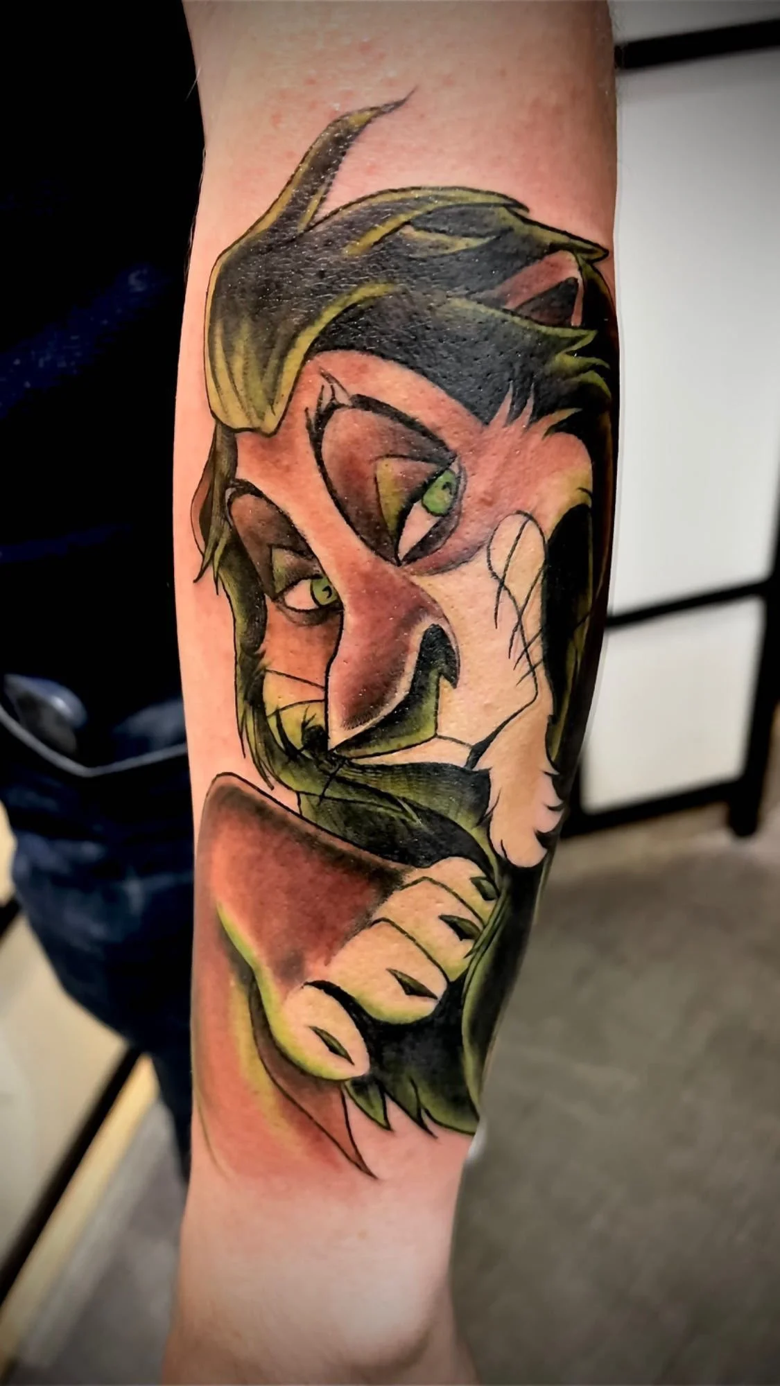 Tatouage cartoon représentant Scar du Roi Lion en couleur sur le bras.