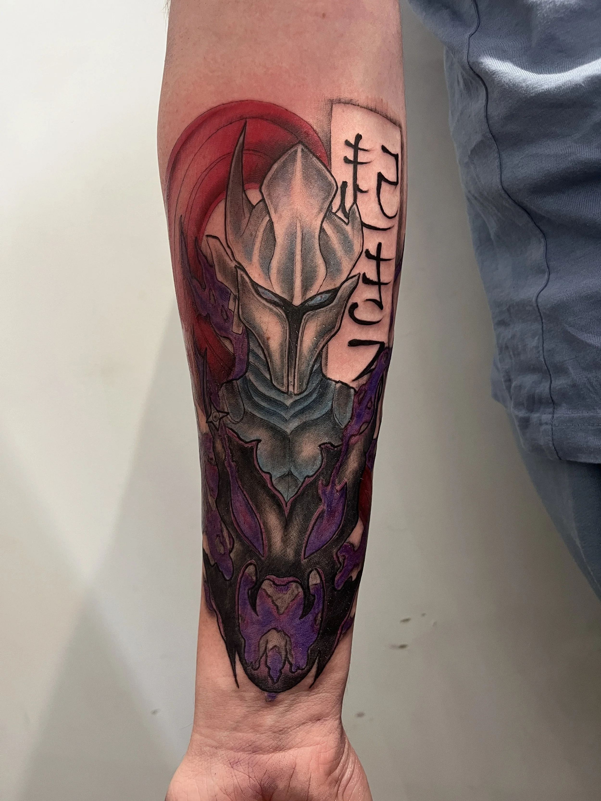 Tatouage manga japonais en couleur représentant un casque de guerrier avec symboles japonais sur le bras.