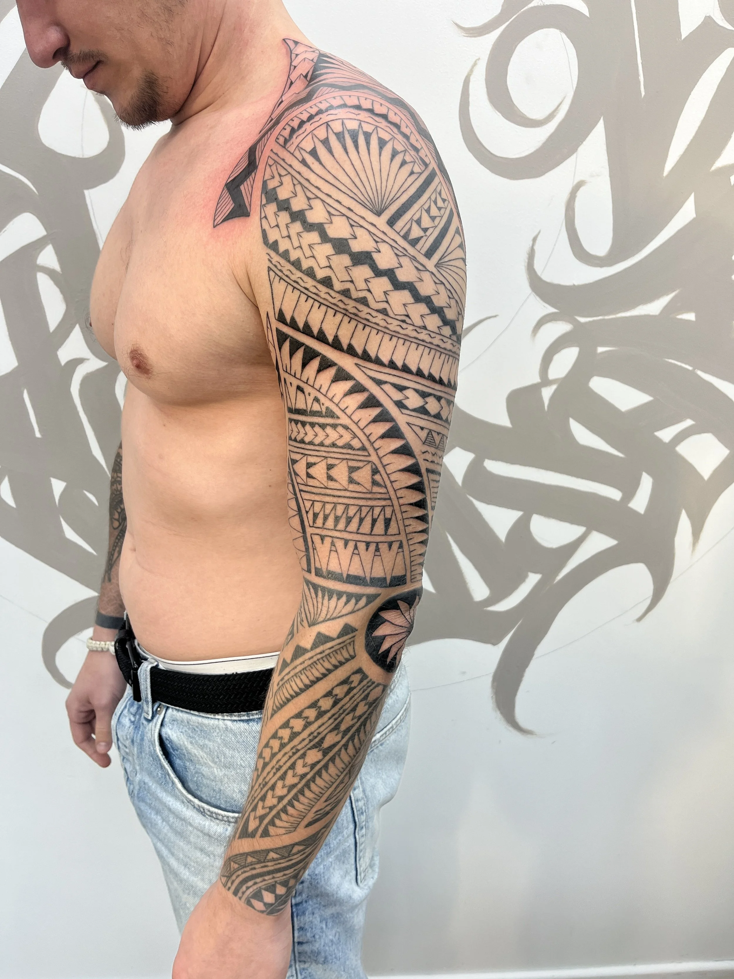 Tatouage polynésien blackwork couvrant le bras avec motifs géométriques et symboles tribaux.