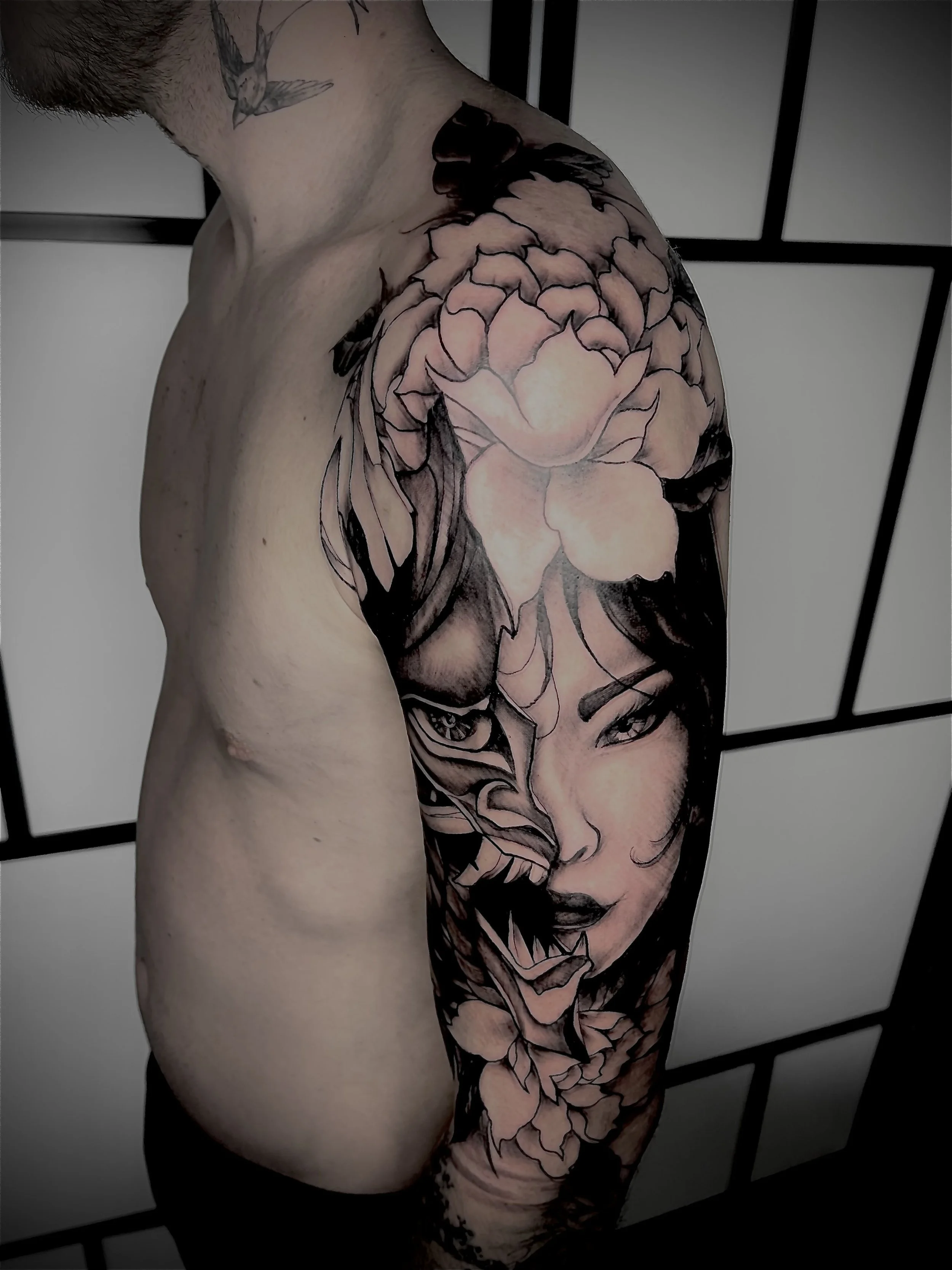 Tatouage japonais représentant un masque Oni fusionné avec un visage de geisha et des fleurs sur le bras.